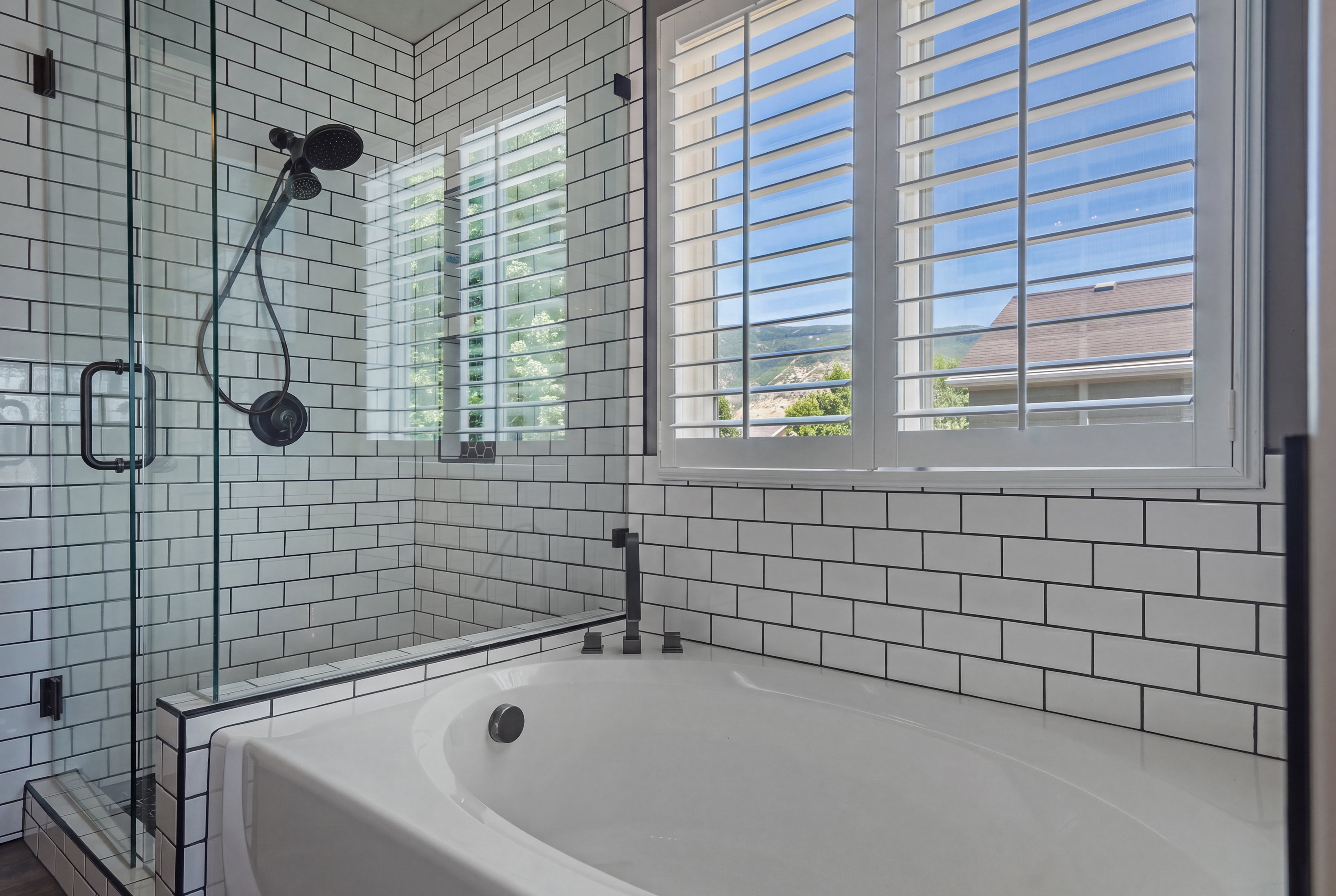 Freestanding soaking tub with dark-finish fixtures, white subway tile surround, and a glass-enclosed shower featuring a dark-finish shower system