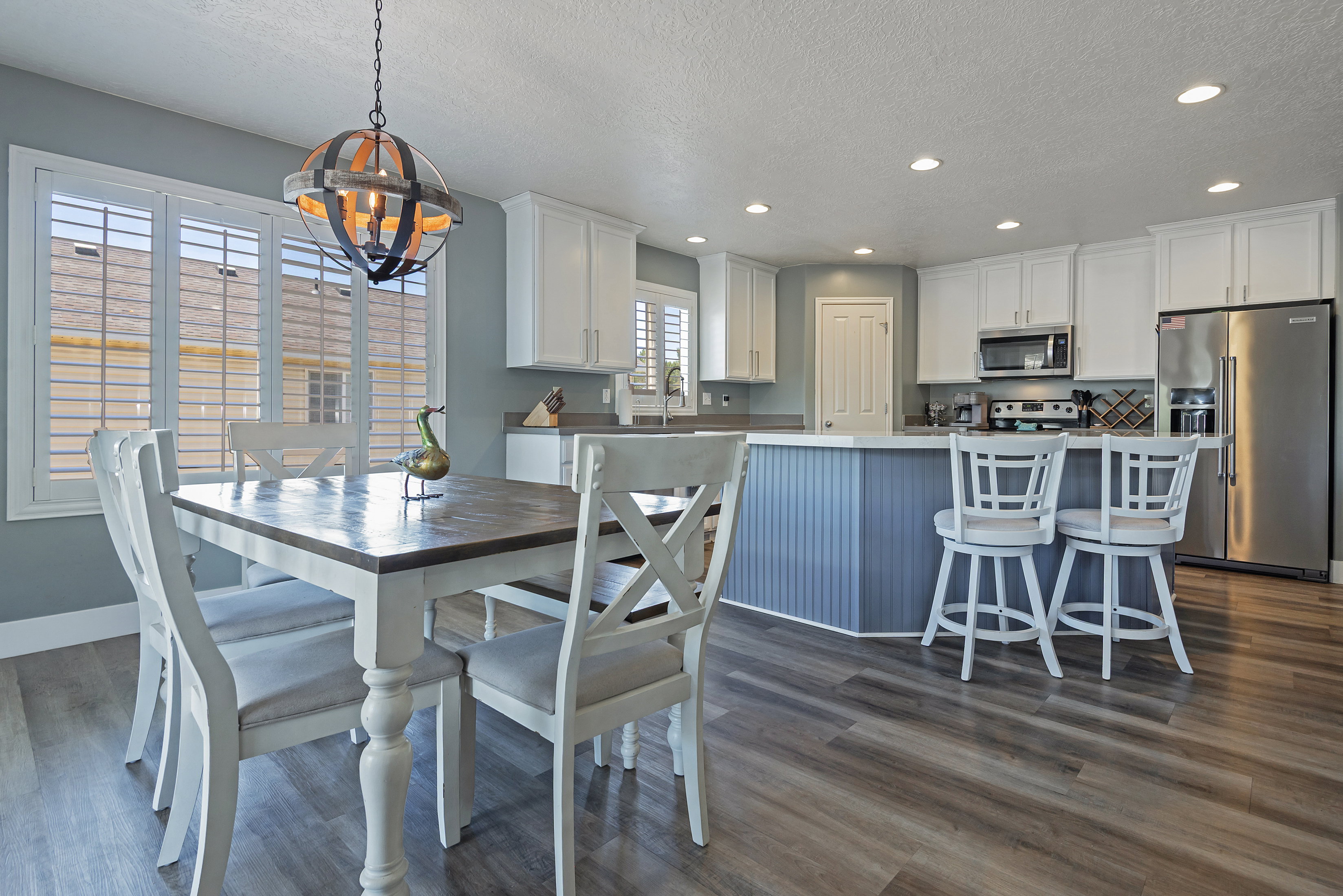Open-concept kitchen and dining area featuring wood-finish flooring, white cabinetry, recessed lighting, stainless steel appliances, and a central island with beadboard paneling