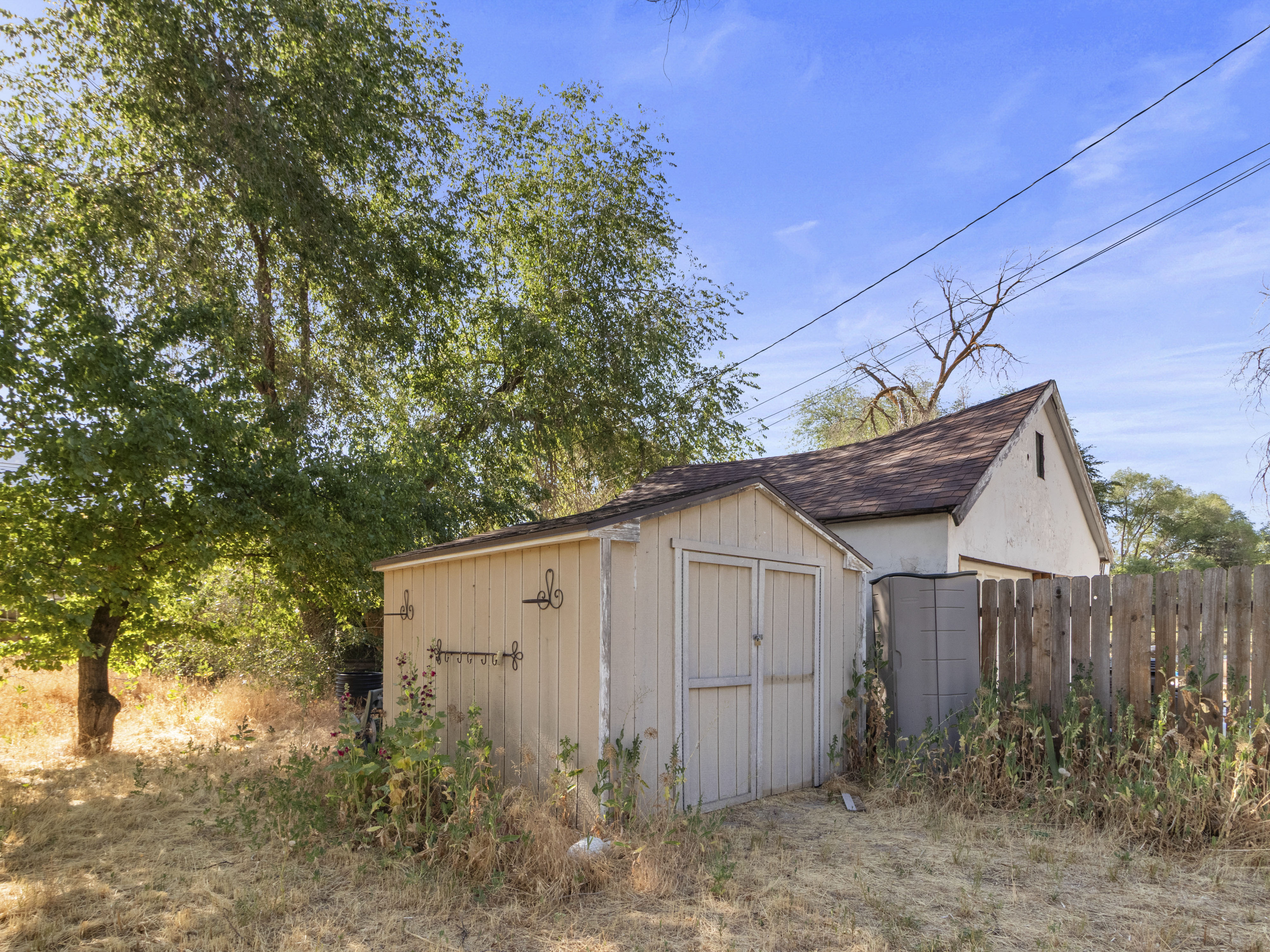 Backyard featuring a detached storage shed, mature trees, and a wood privacy fence