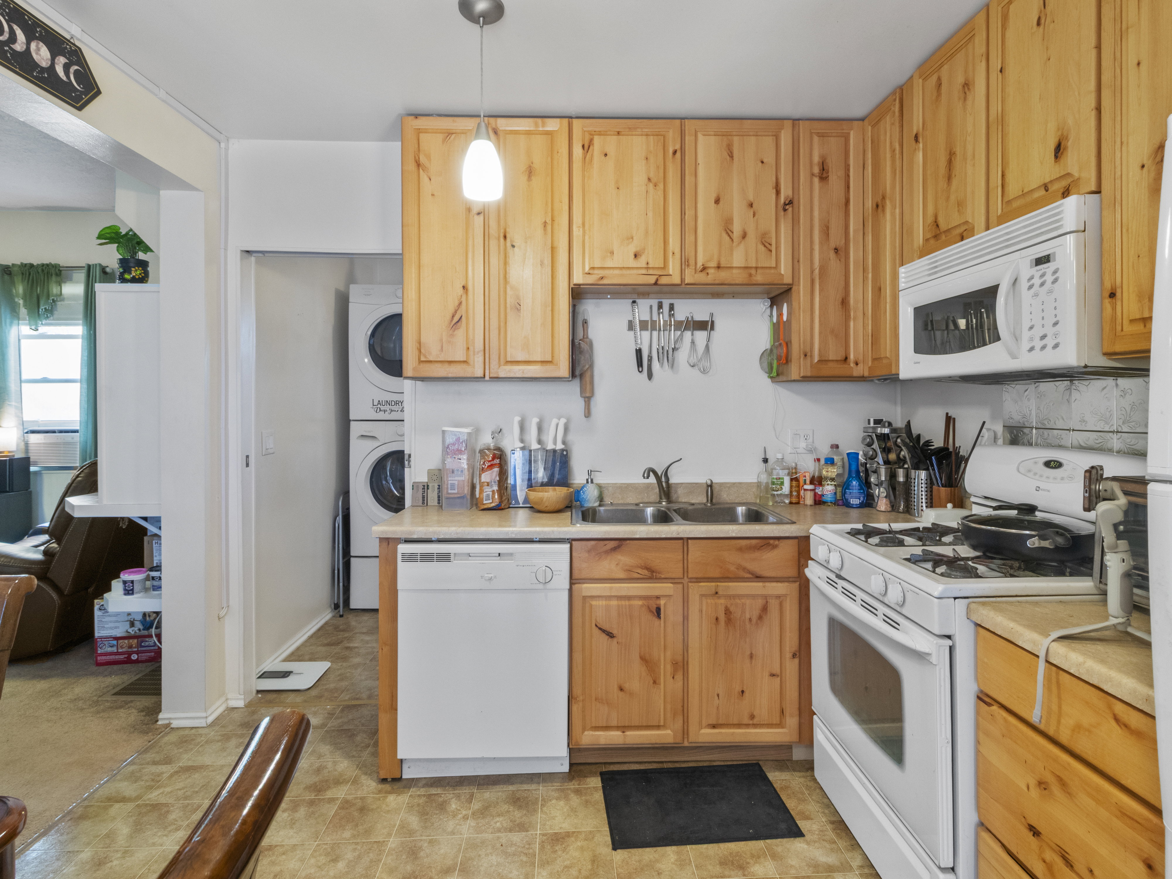 Kitchen featuring wood cabinetry, laminate countertops, a double basin sink, and a white appliance suite including a dishwasher, range, and microwave