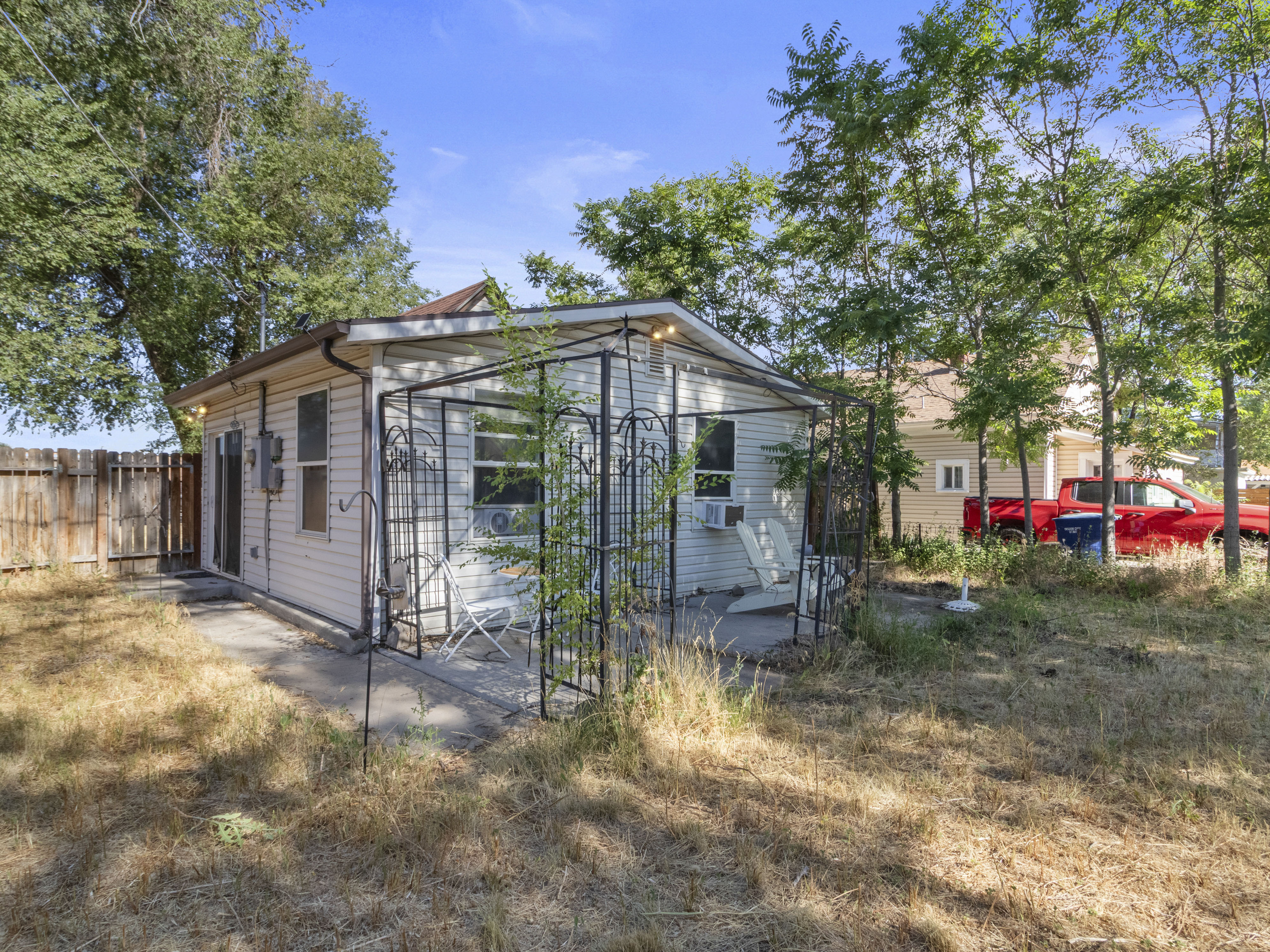 Rear exterior featuring white horizontal siding, a private patio area, a dark metal pergola, and a wooden fence boundary