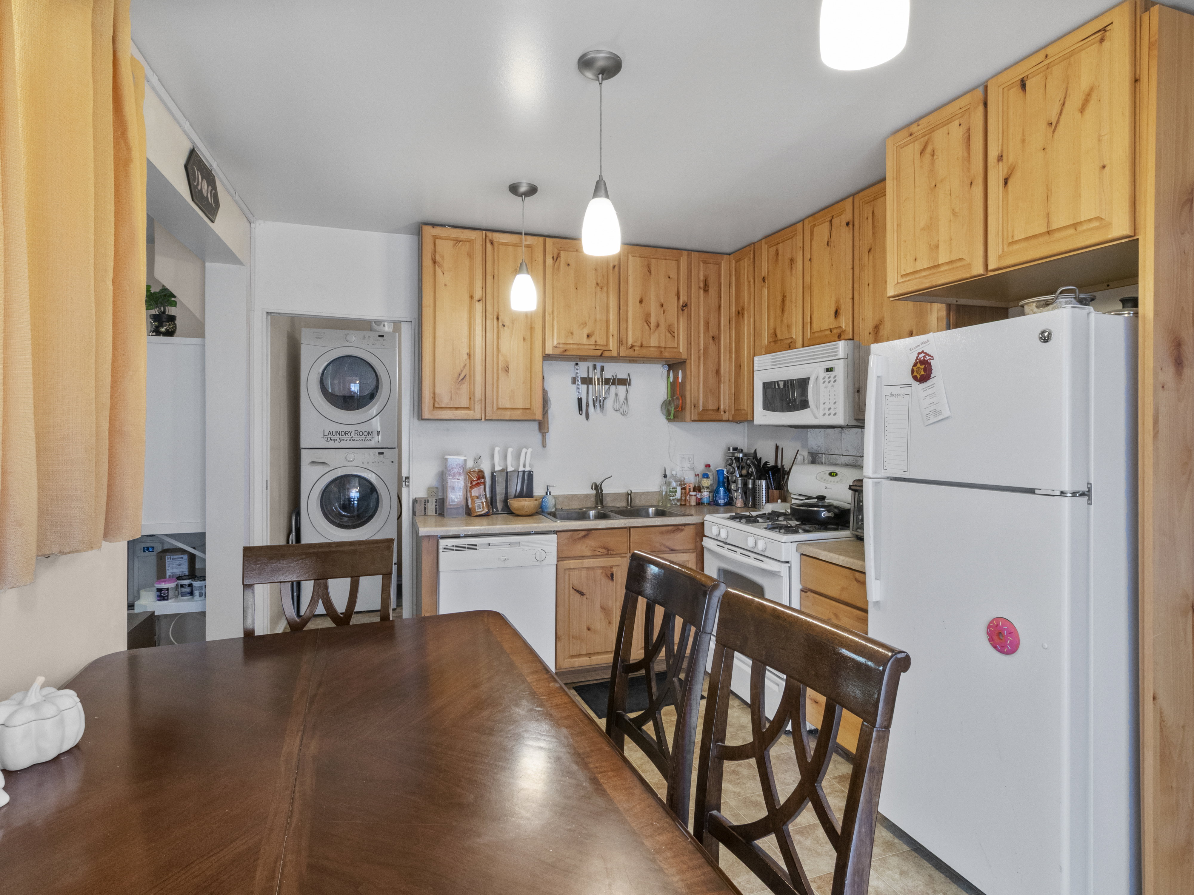 Kitchen and dining area featuring wood-finish cabinetry, white appliances, a built-in microwave, and a stackable washer and dryer unit