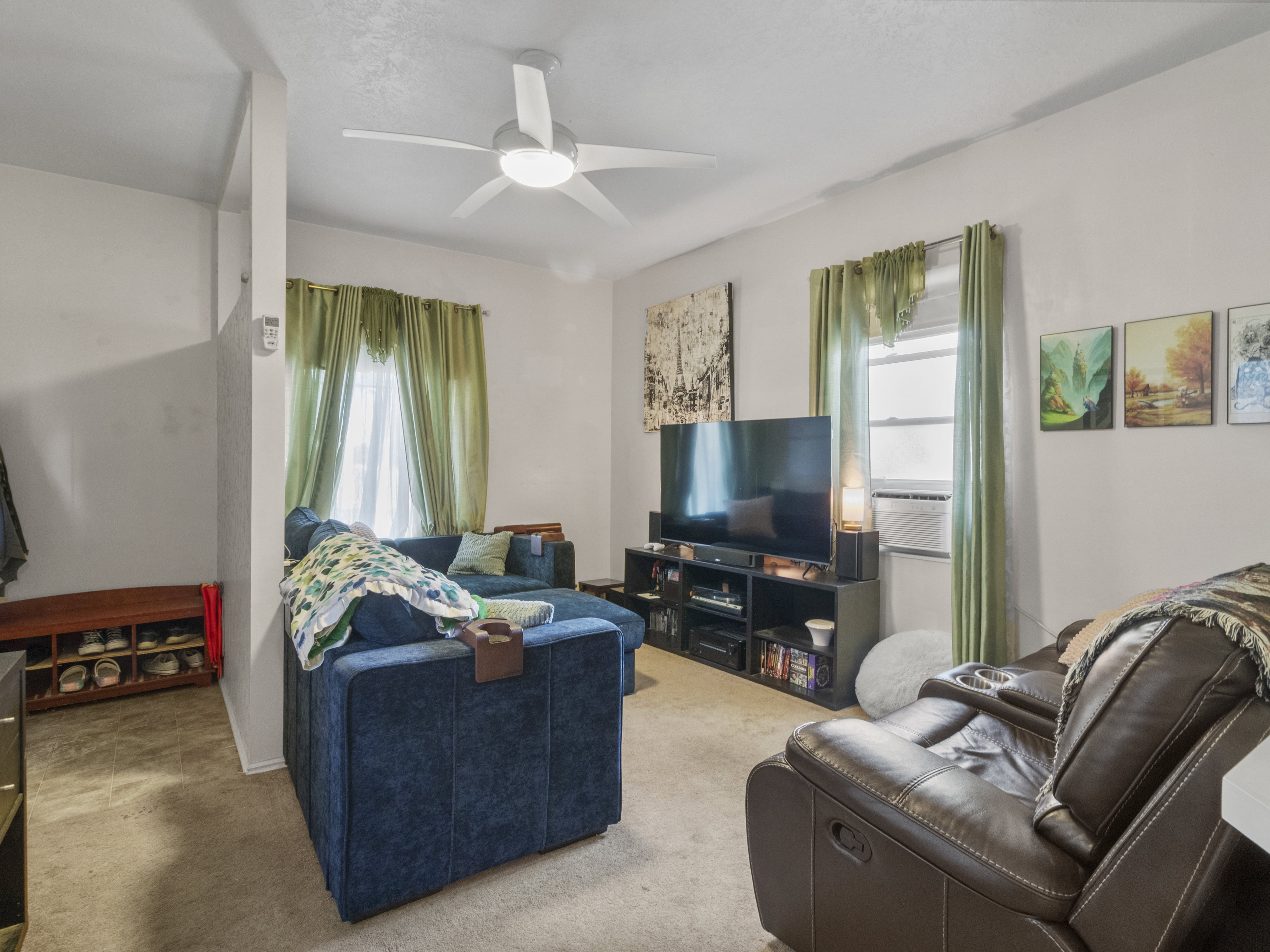 Living area with neutral carpeting, white walls, and a ceiling fan with integrated lighting
