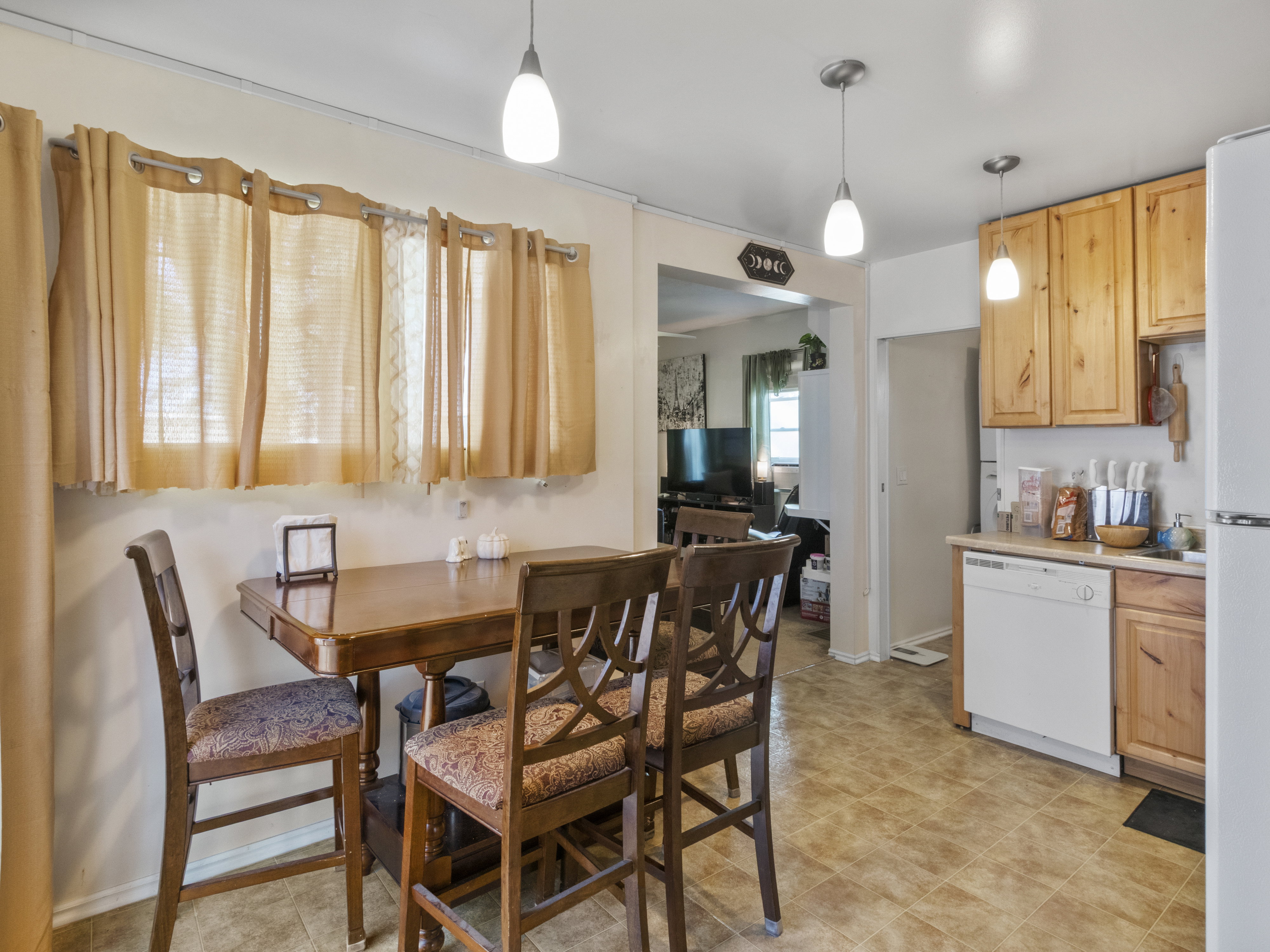 Kitchen area with wood-finish cabinetry, white dishwasher, and pendant lighting fixtures