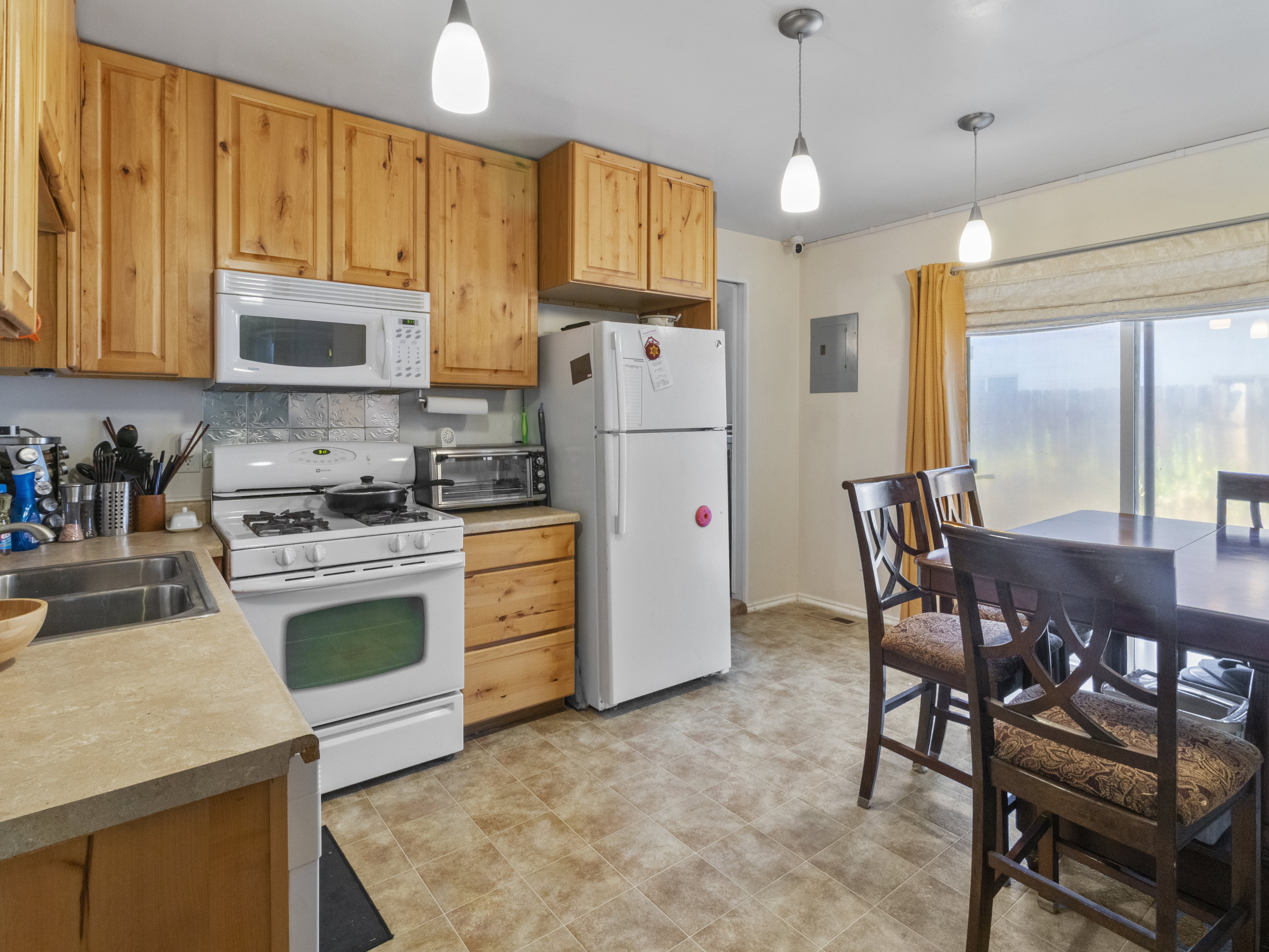 Kitchen and dining area featuring wood-finish cabinetry, a white gas range with an overhead microwave, and a double basin stainless steel sink