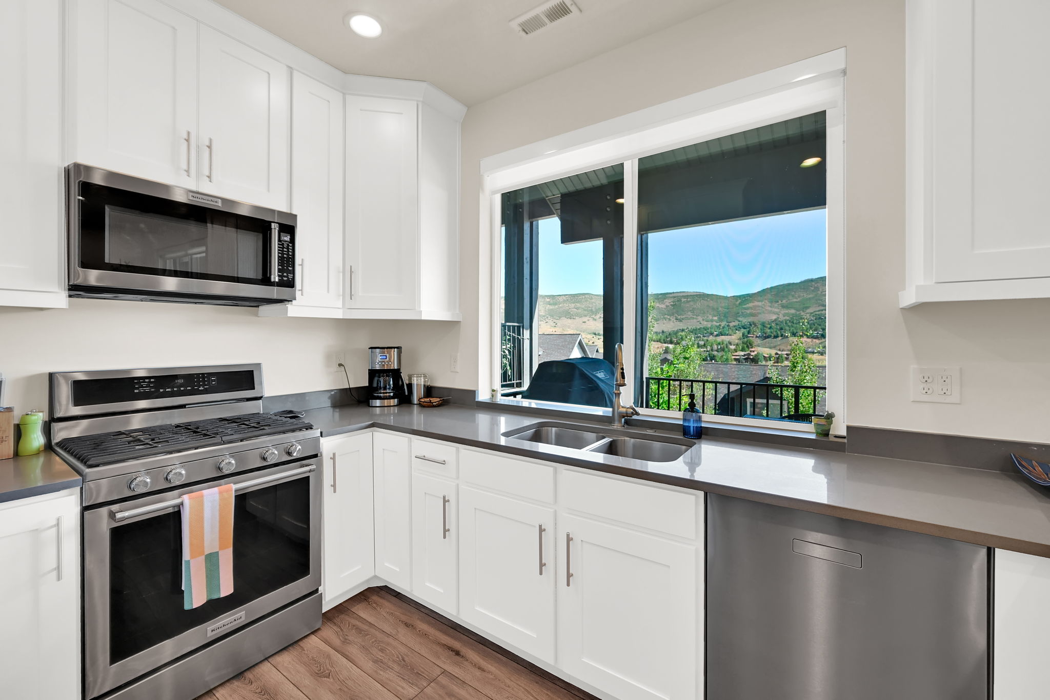 Kitchen featuring white shaker cabinetry, stainless steel appliances, wood-finish flooring, and a large window overlooking a mountain landscape