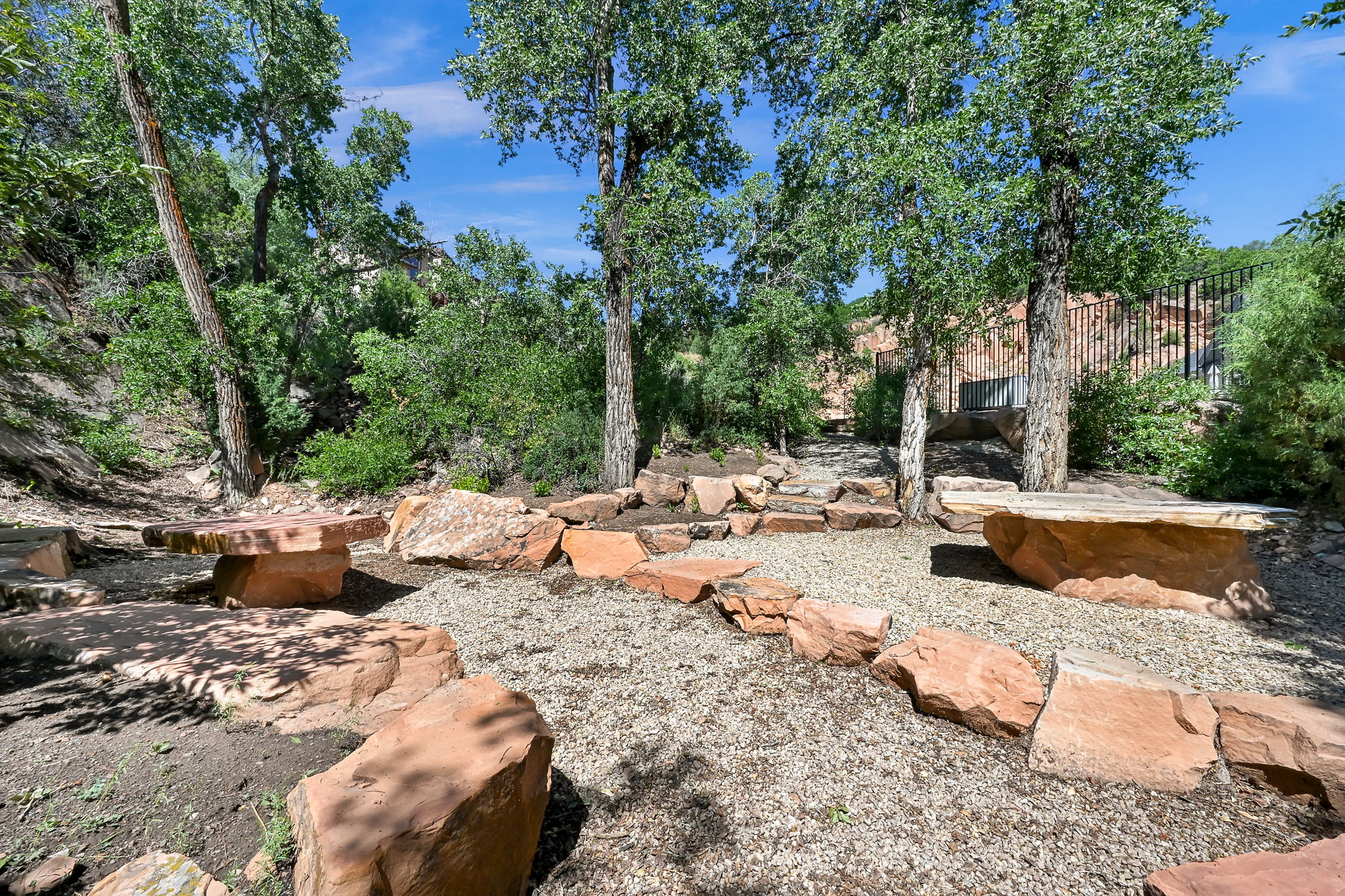 Landscaped outdoor area featuring natural stone seating, gravel ground cover, mature trees, and a sloped terrain