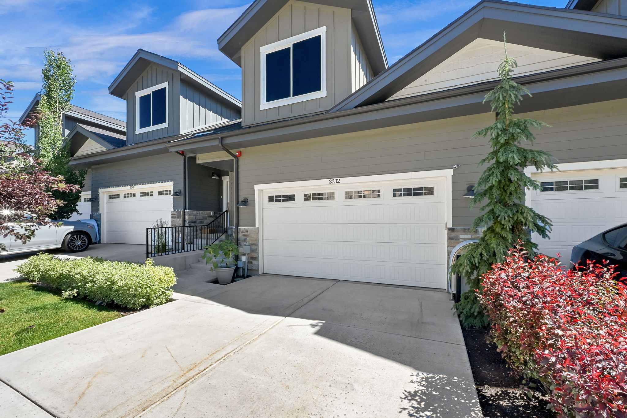 Modern townhome exterior featuring gray siding, white garage doors with window inserts, stone accents, and manicured landscaping