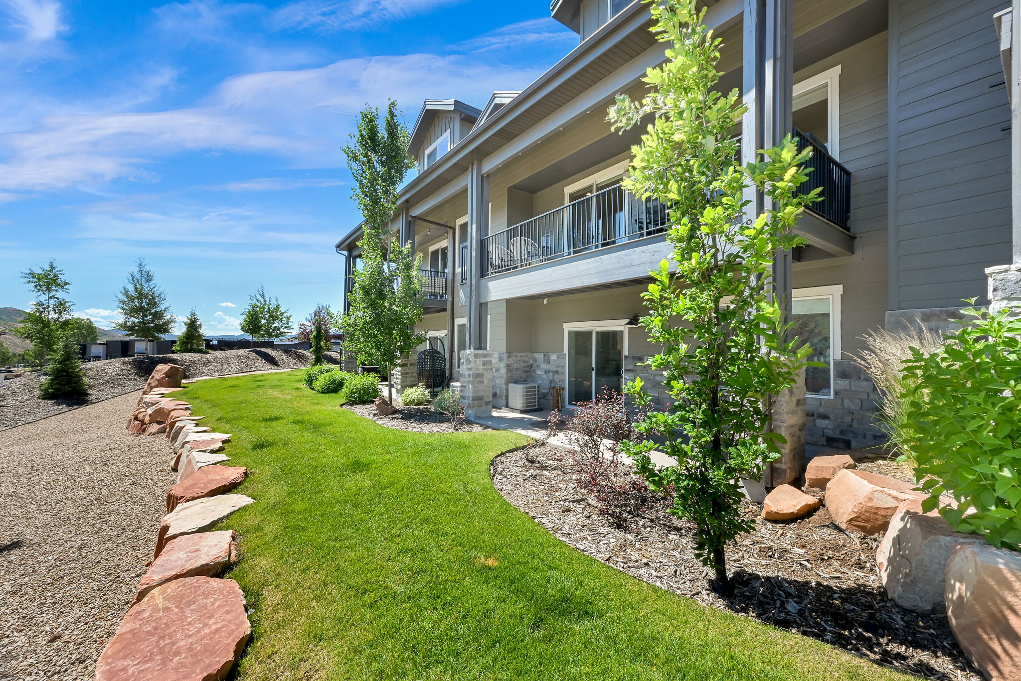 Exterior featuring multiple private balconies with black metal railings, a stone accent facade, and a lower-level patio with sliding glass doors
