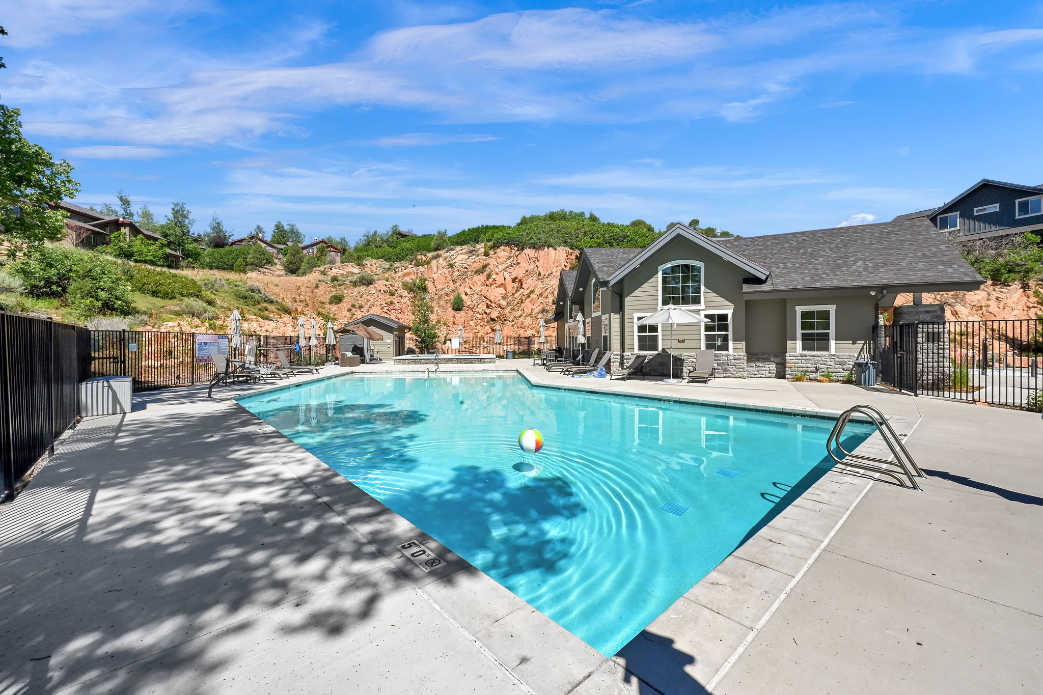 Outdoor swimming pool with concrete surround, bordered by black metal fencing and a multi-level building with stone accent siding