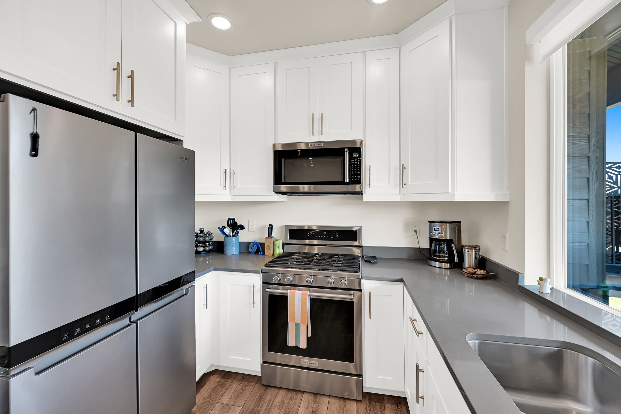 Modern kitchen featuring white shaker cabinetry, stainless steel appliances, a corner gas range, a large stainless steel sink, and wood-finish flooring