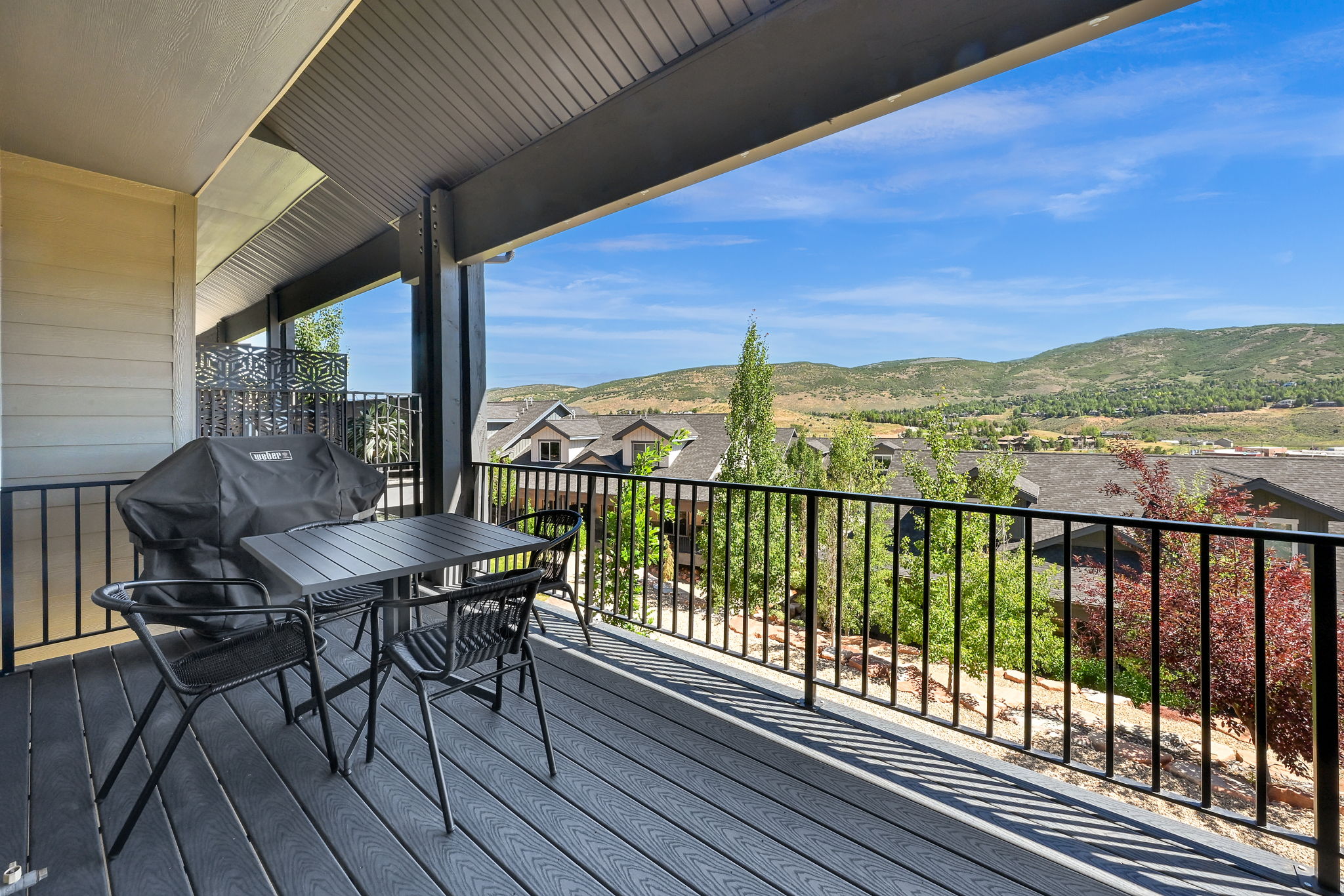 Covered deck featuring composite wood-finish flooring, black metal railings, and an expansive mountain backdrop