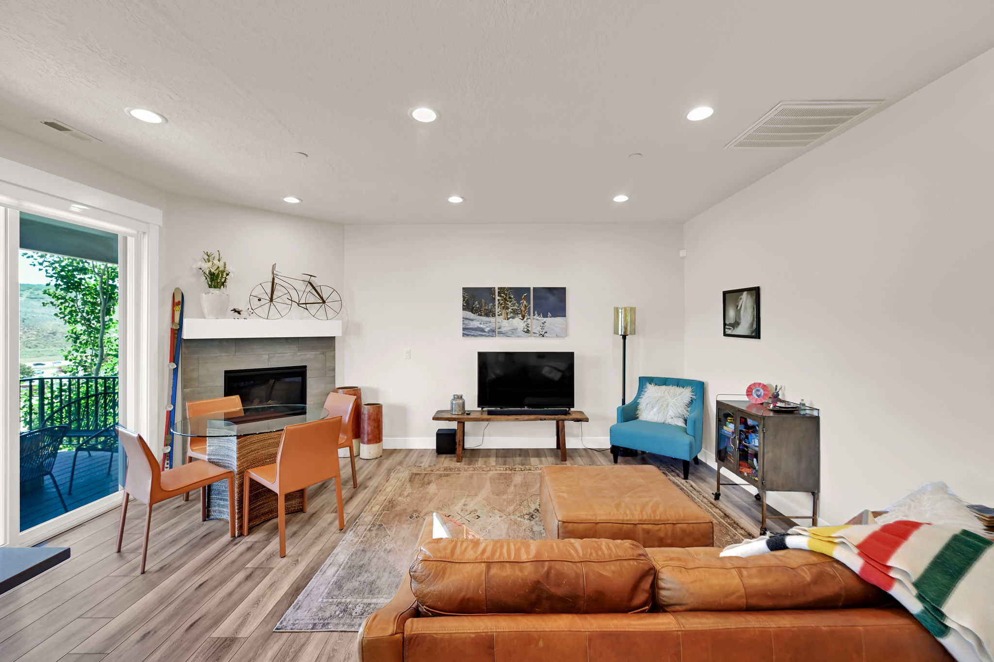 Living area featuring wood-finish flooring, a fireplace with a stone surround and white mantel, recessed lighting, and a sliding glass door opening to an outdoor balcony