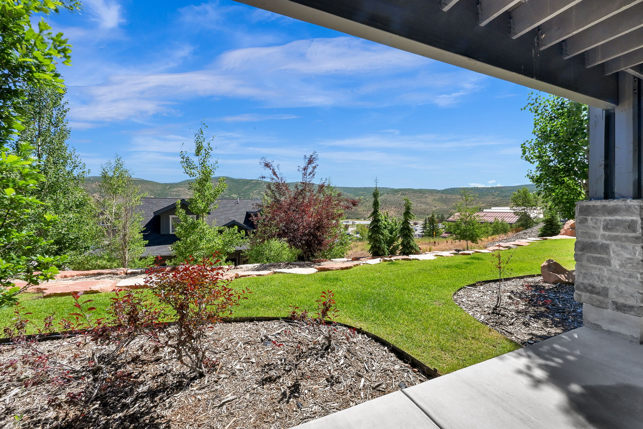 Expansive outdoor living area featuring a stone column, concrete patio, and a terraced lawn