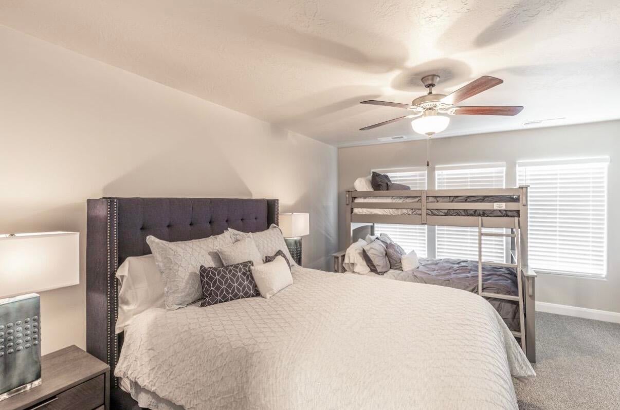 Spacious room featuring light gray wall paint, textured carpet flooring, and a ceiling fan with integrated lighting