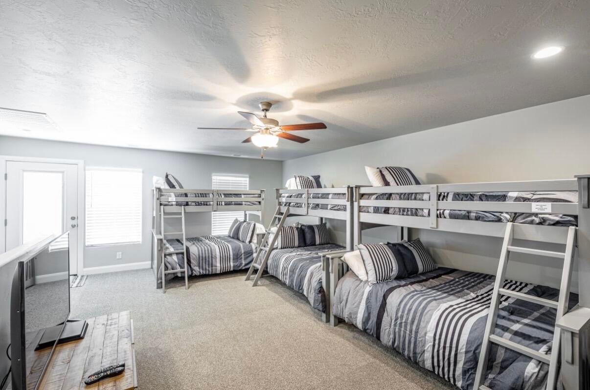 Spacious room featuring multiple bunk beds, neutral tone carpeting, a ceiling fan, recessed lighting, and a white door with an adjacent window