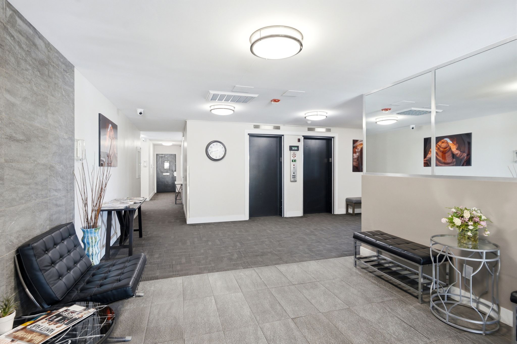 Lobby area featuring tile flooring, two elevators, a mirrored wall, and a textured accent wall