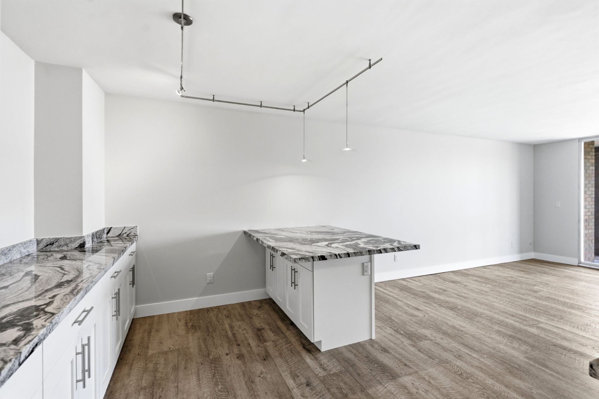 Kitchen area featuring white shaker-style cabinetry with silver-tone hardware, stone countertops with a striking veined pattern, and wood-finish flooring