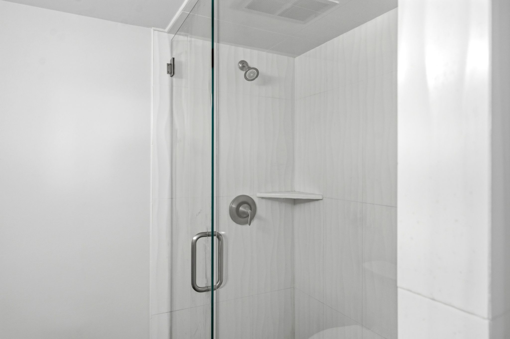 Glass-enclosed shower with a brushed nickel shower head, control handle, and a built-in corner shelf