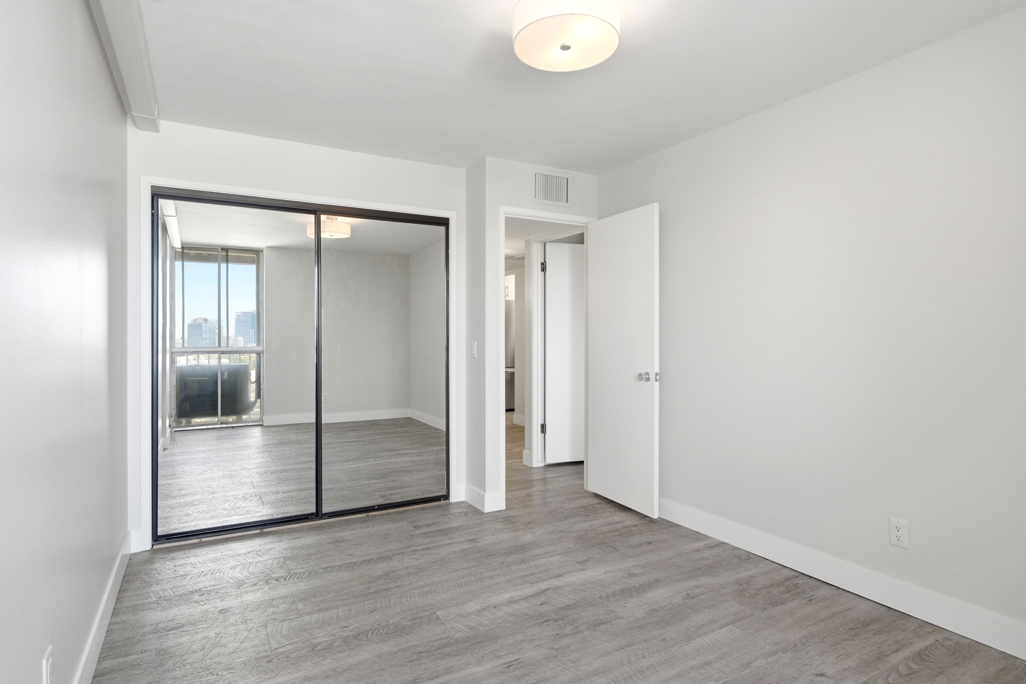 Expansive room featuring wood-finish flooring, light grey walls, white baseboards, and a semi-flush ceiling light fixture