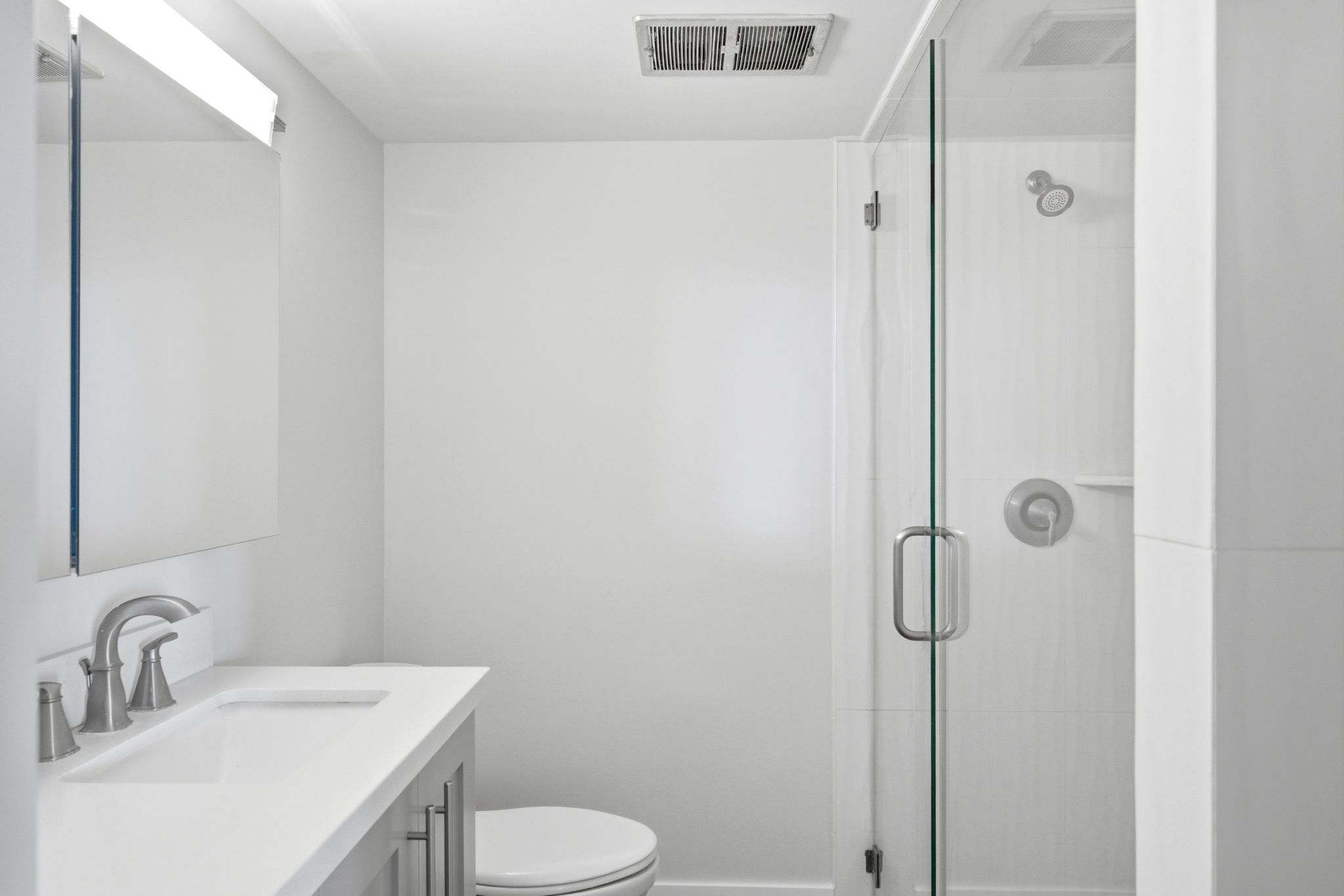 Bathroom featuring a glass-enclosed shower, white tile surround, brushed nickel fixtures, a single vanity with a white countertop, and a wall-mounted mirror