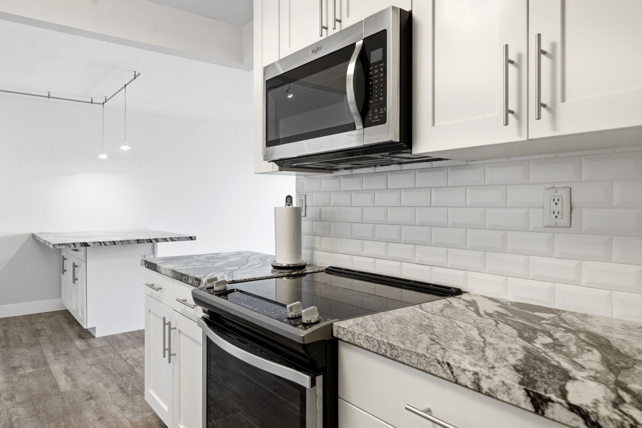 Kitchen featuring white cabinetry, stainless steel microwave, integrated electric cooktop, light-toned countertop with dark veining, and white subway tile backsplash