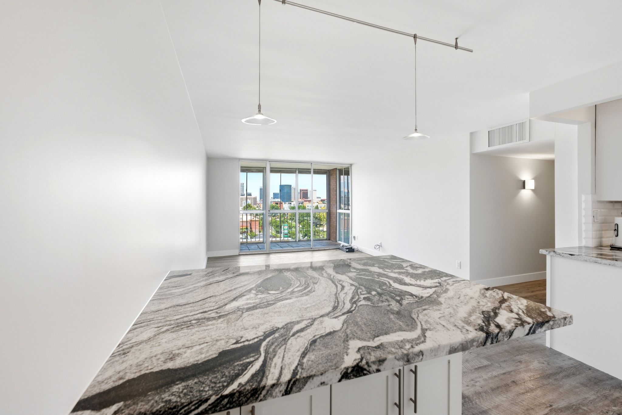 Spacious open-concept living area featuring an expansive kitchen island with a striking natural stone countertop, pendant lighting, and wood-finish flooring