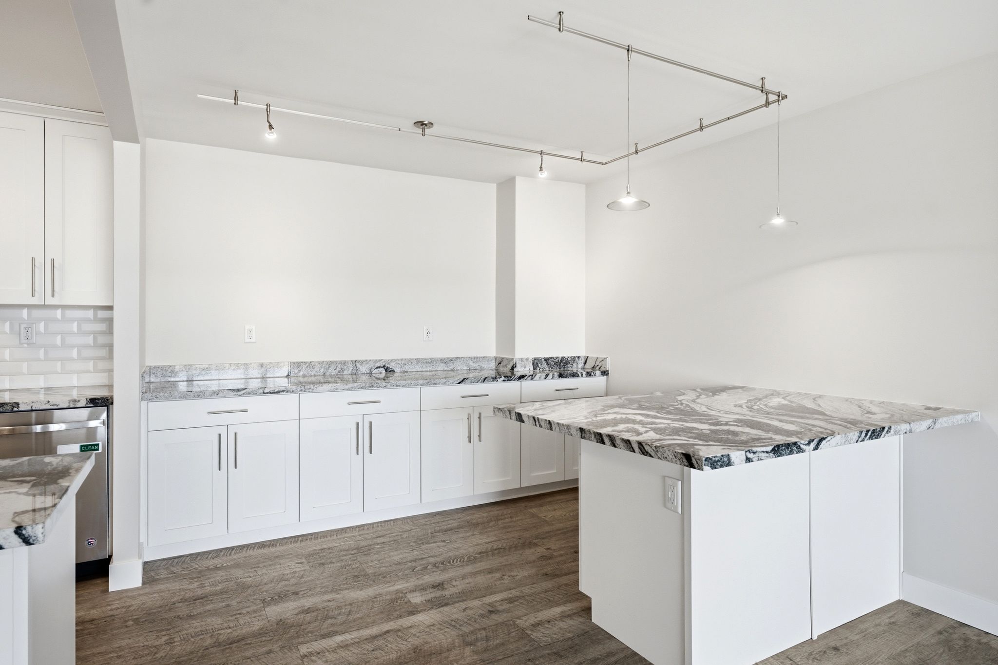 Expansive kitchen featuring a large central island with a waterfall-edge countertop, white shaker-style cabinetry, and wood-finish flooring