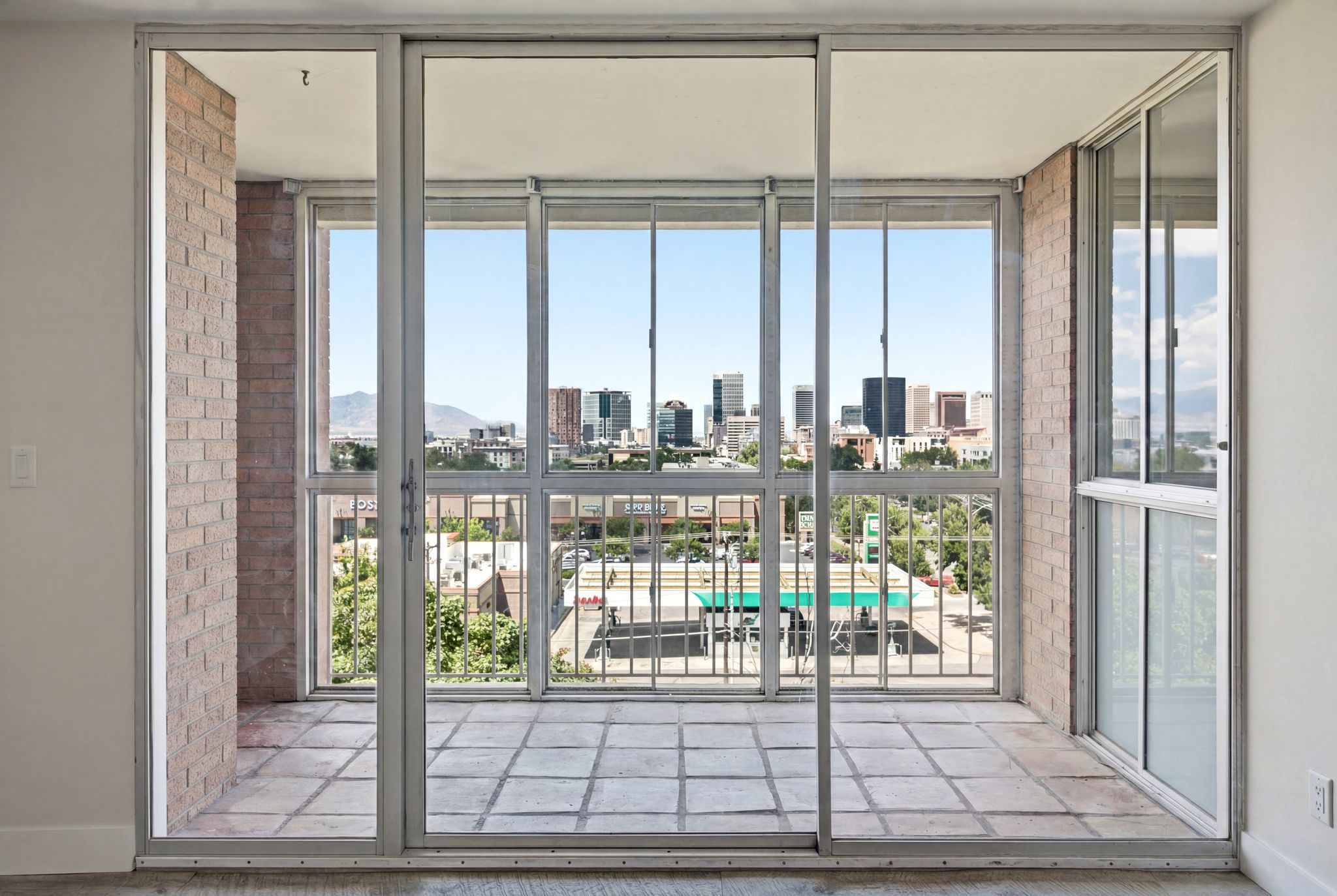 Sliding glass doors opening to an outdoor patio with tiled flooring and a brick-finish wall