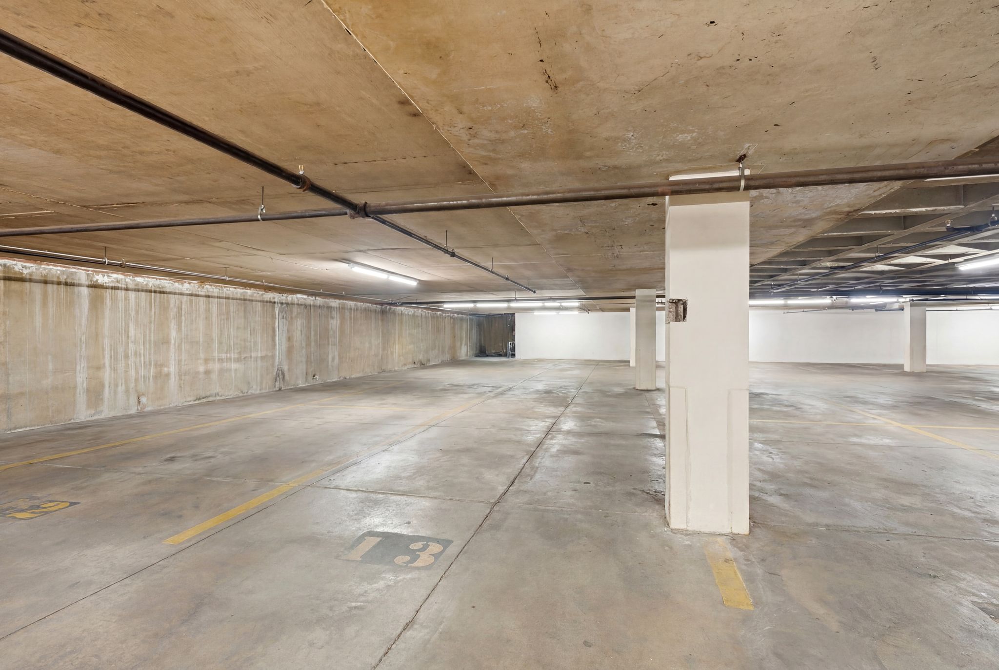Spacious concrete parking garage with overhead exposed piping and fluorescent lighting