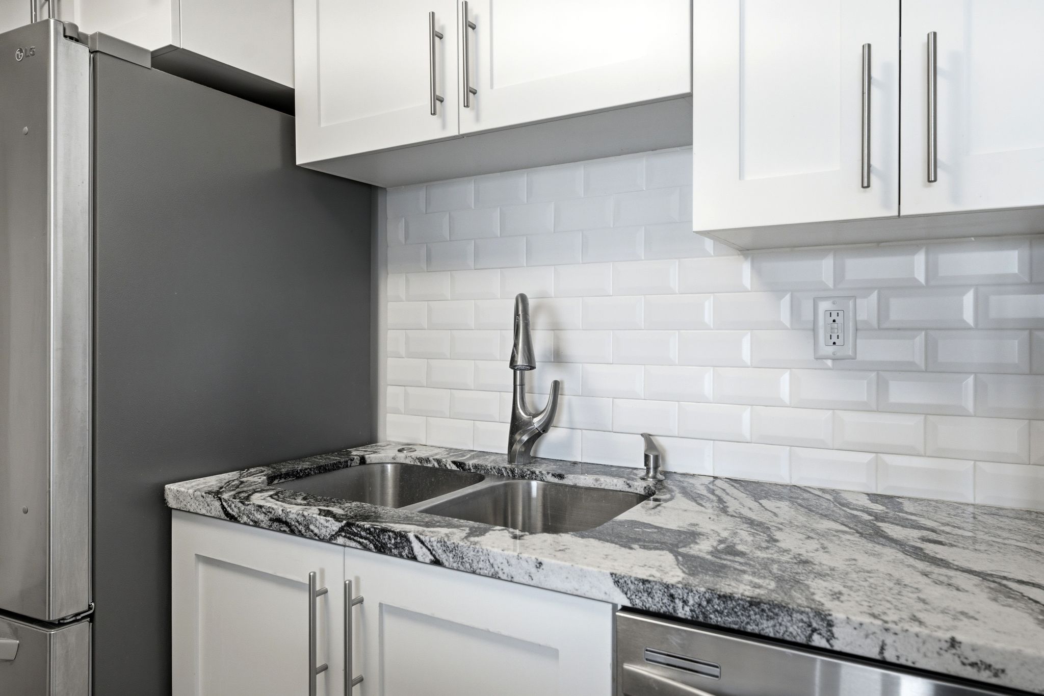 Kitchen featuring white shaker-style cabinetry with brushed nickel hardware, a dual basin stainless steel sink, and a high-arc faucet