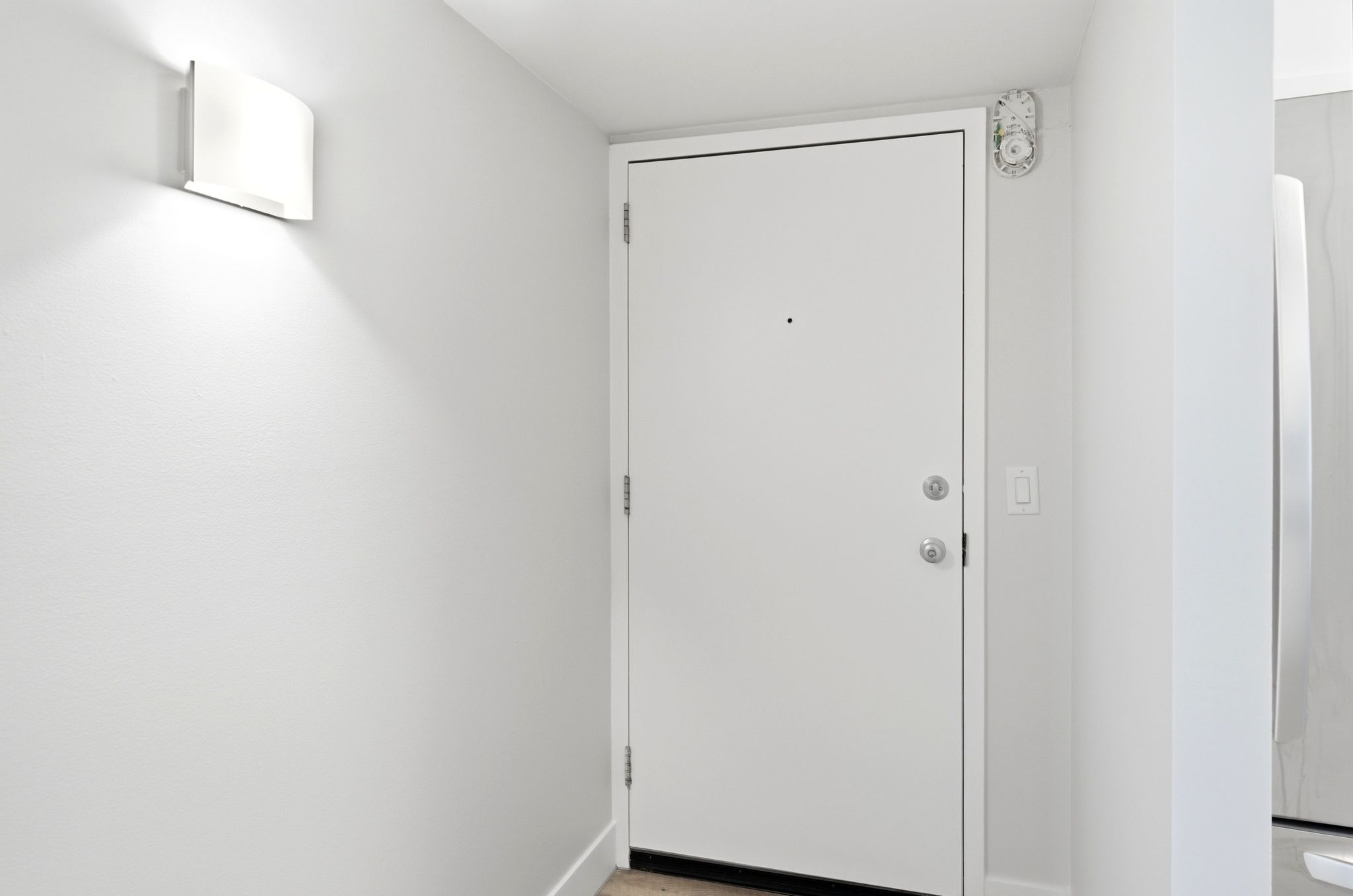 White entry door with satin nickel hardware and a wall-mounted sconce