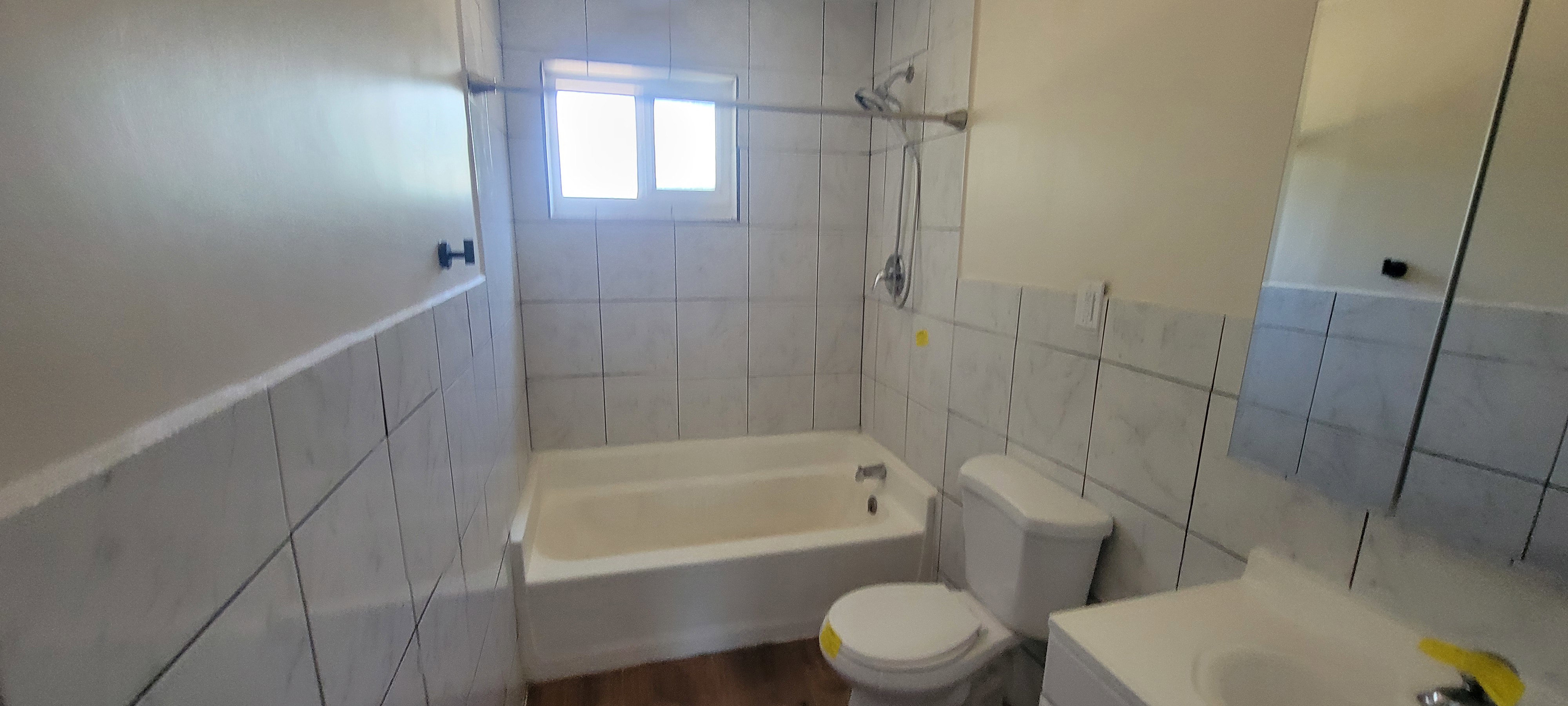 Bathroom featuring white wall tile, a white bathtub with shower fixture, a window with frosted glass, and wood-finish flooring