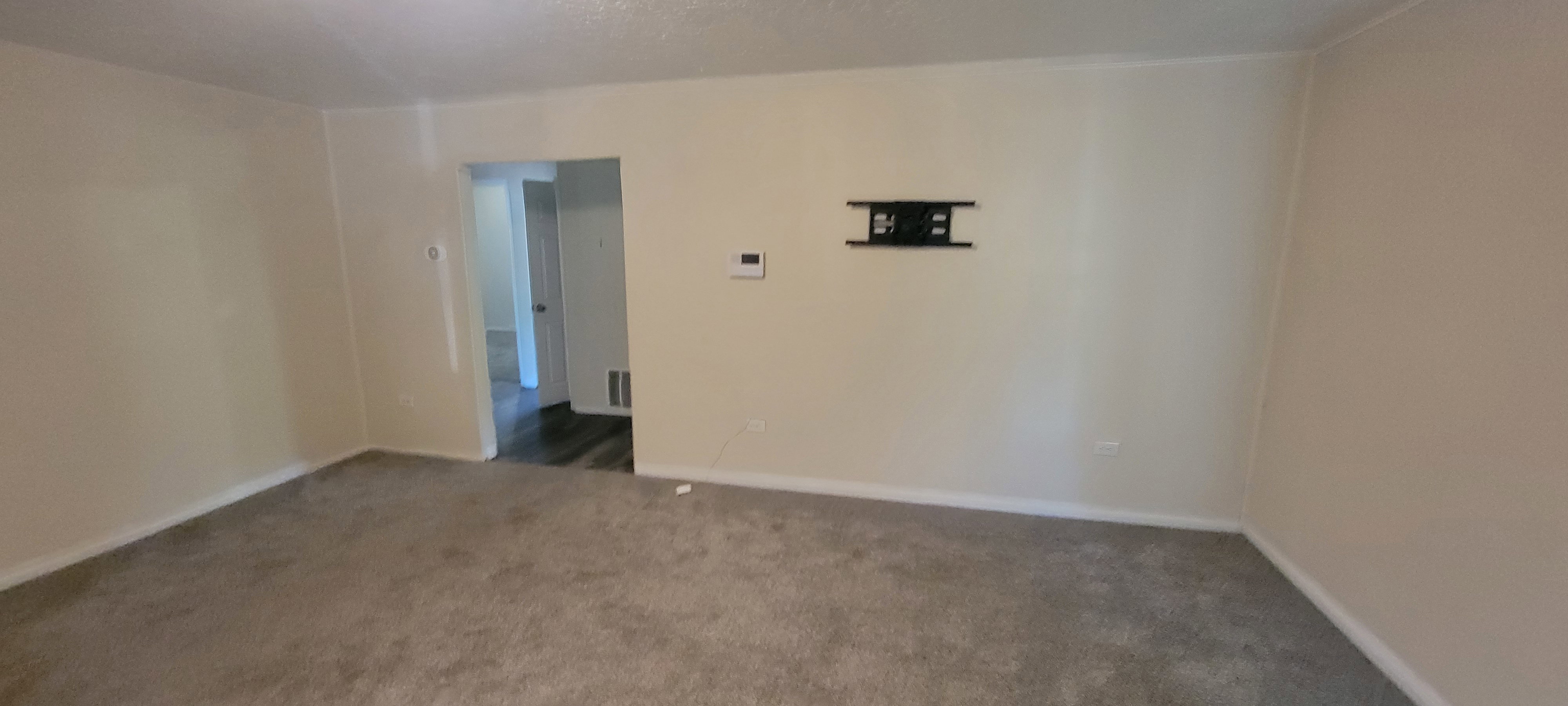 Living space featuring neutral wall paint, light-colored carpeting, white trim, and a wall-mounted bracket