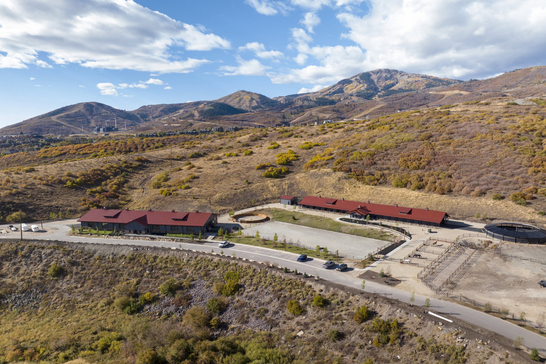 Sprawling equestrian facility featuring multiple structures with red roofs, extensive outdoor riding arenas, fenced paddocks, and a round pen