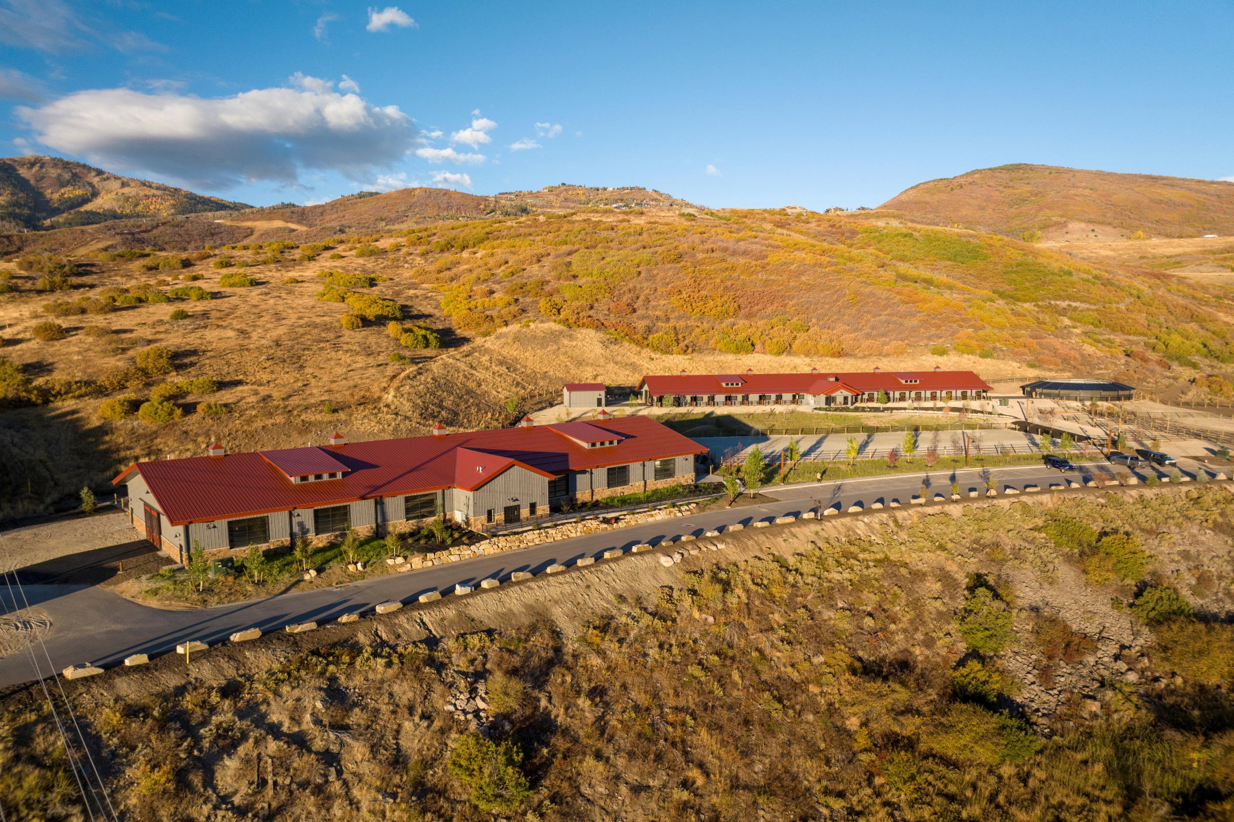Expansive property featuring two structures with red metal roofs and gray siding, set against a mountainous backdrop