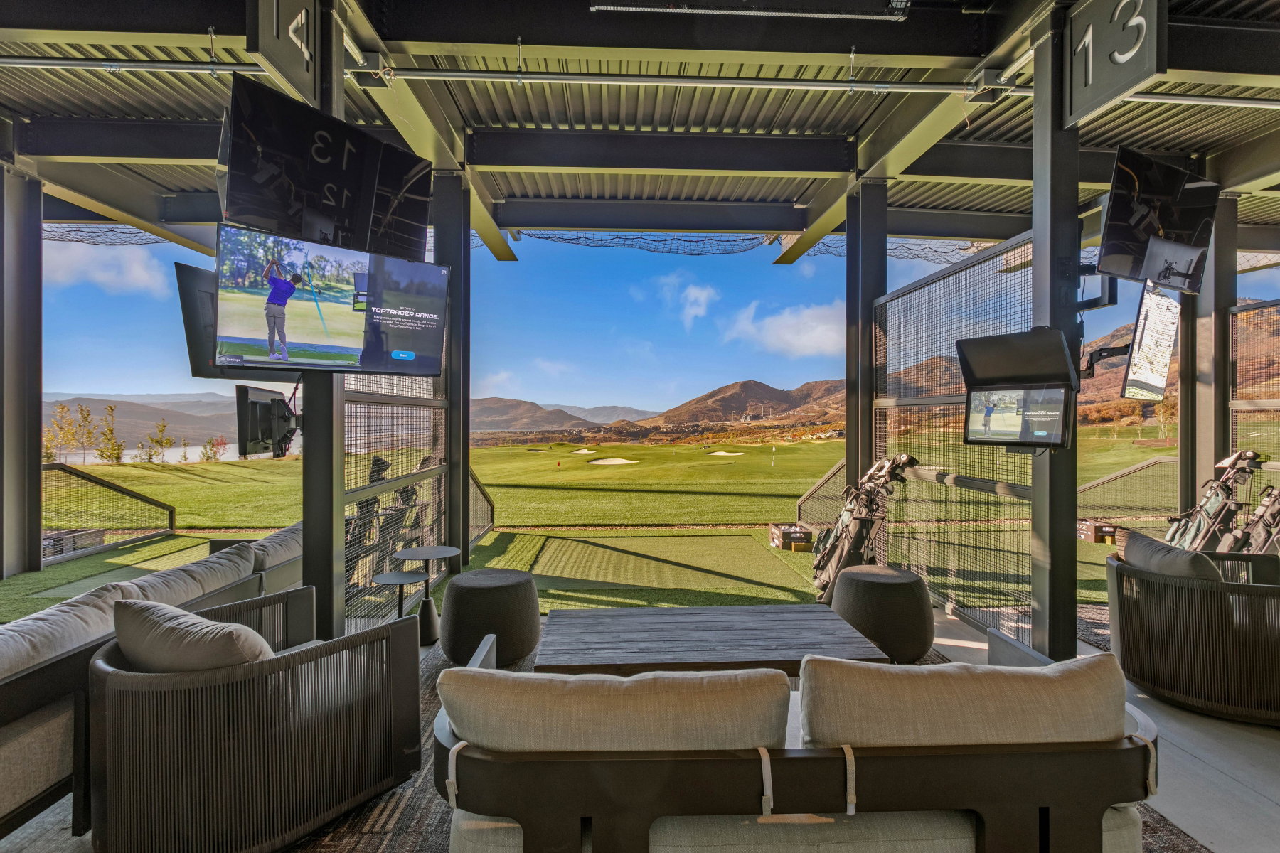 Outdoor golf lounge featuring multiple screens, a turf-covered floor, and distant mountain scenery