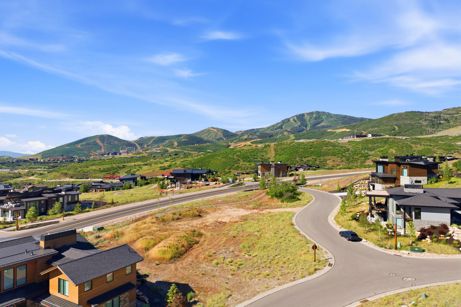 Mountainous landscape featuring multiple properties with modern architecture, paved roads, and lush green hills