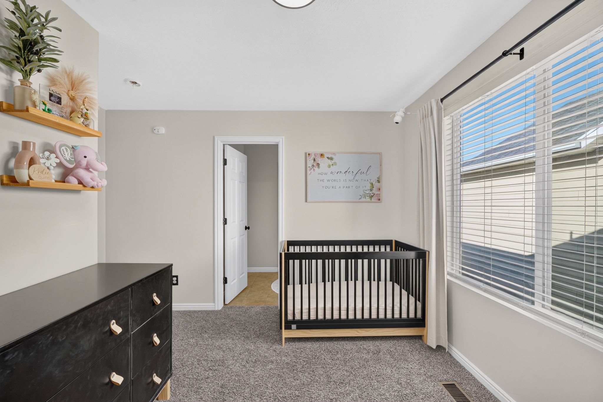 Carpeted room featuring neutral wall tones, a large window with blinds, and a standard door frame