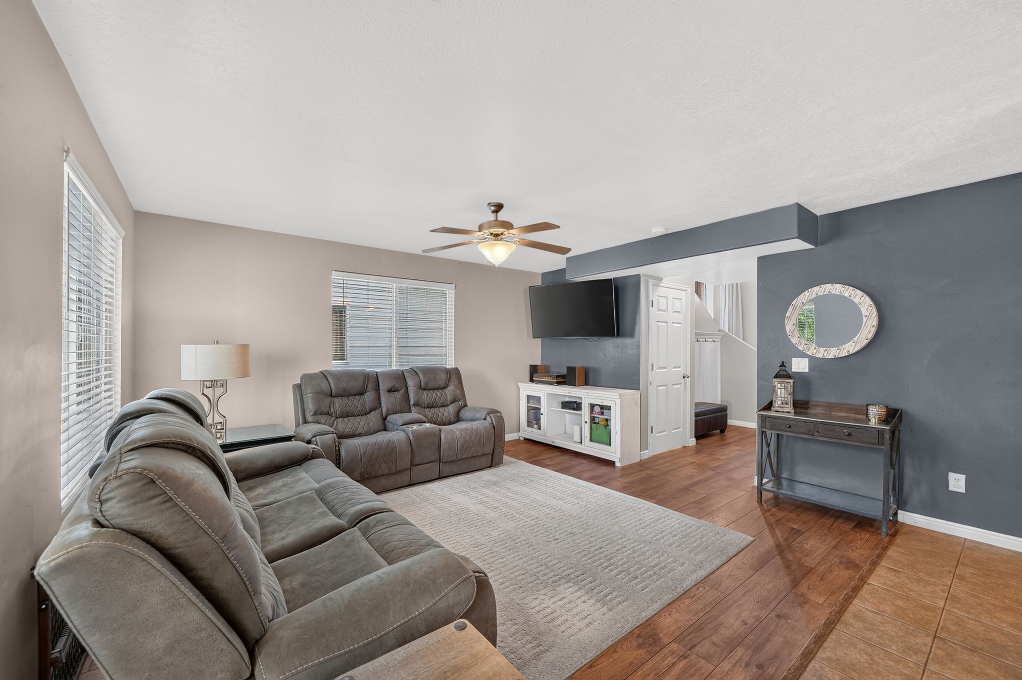 Living space featuring wood-finish flooring, two windows with blinds, and a ceiling fan with integrated lighting