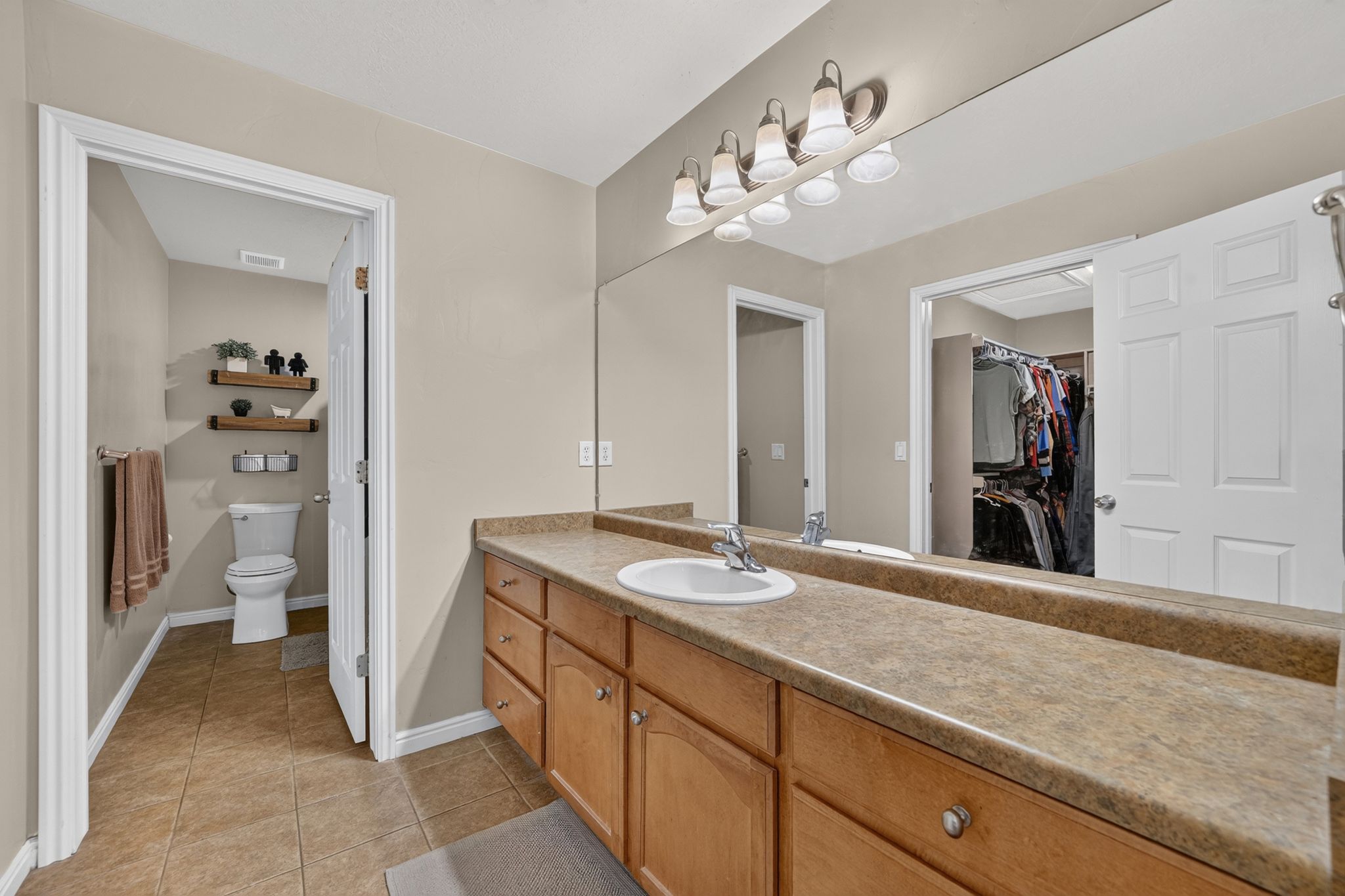 Bathroom vanity featuring extensive counter space with a single sink, wood-finish cabinetry, and a large wall-mounted mirror