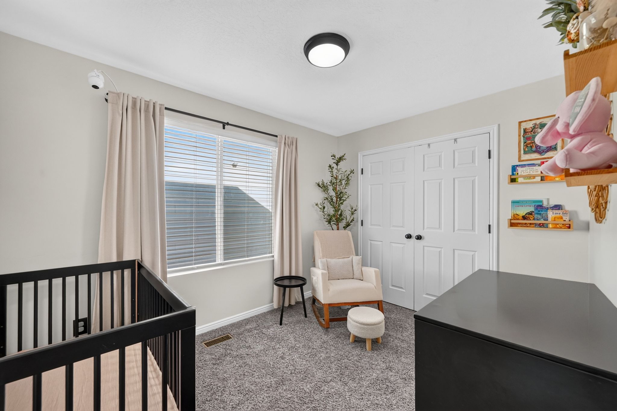 Carpeted room featuring a large window with blinds and drapes, a flush-mount ceiling light fixture, and double bi-fold closet doors with black hardware
