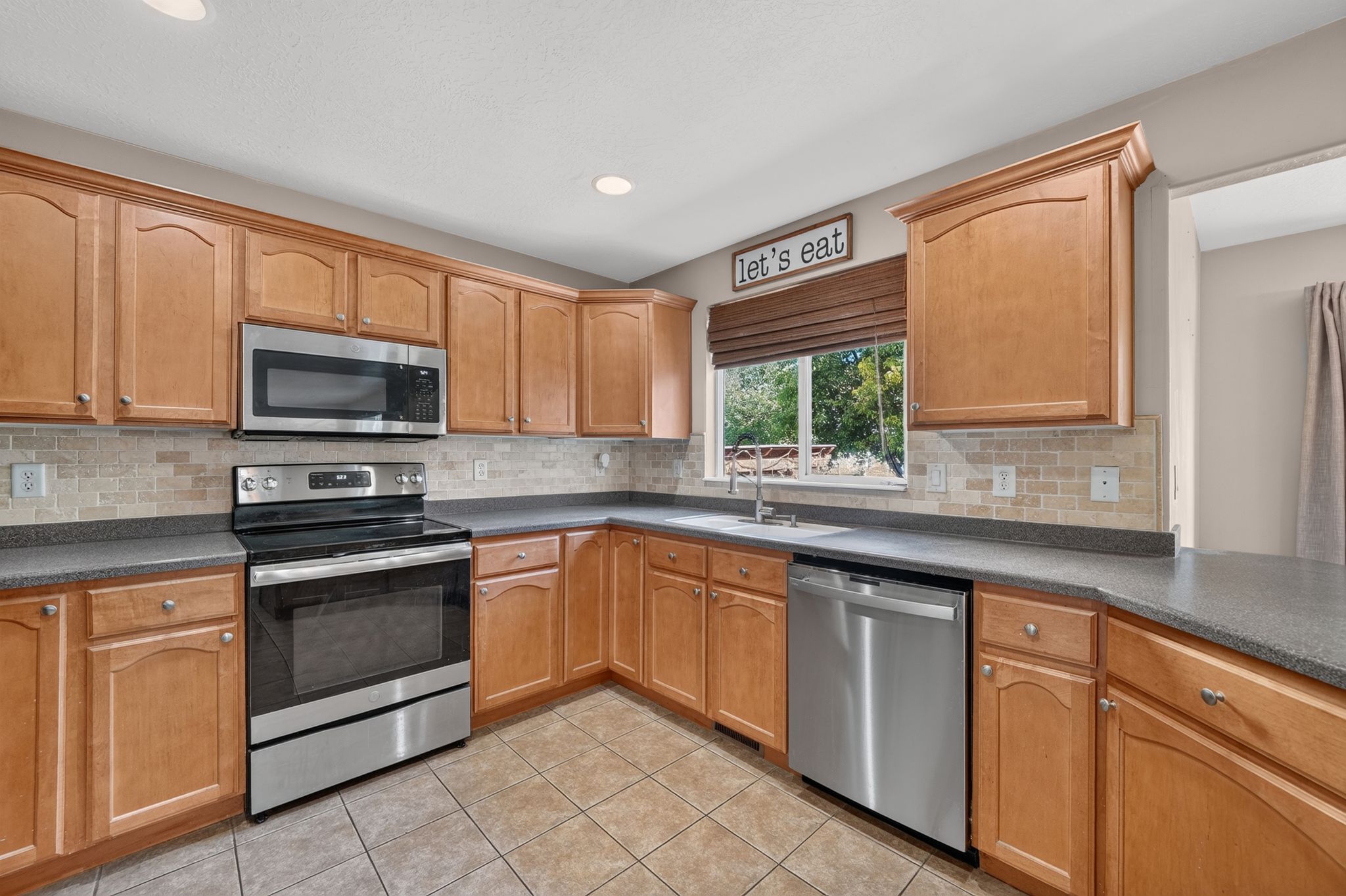 Kitchen featuring wood cabinetry, stainless steel appliances, a tile backsplash, dark countertops, and tile flooring