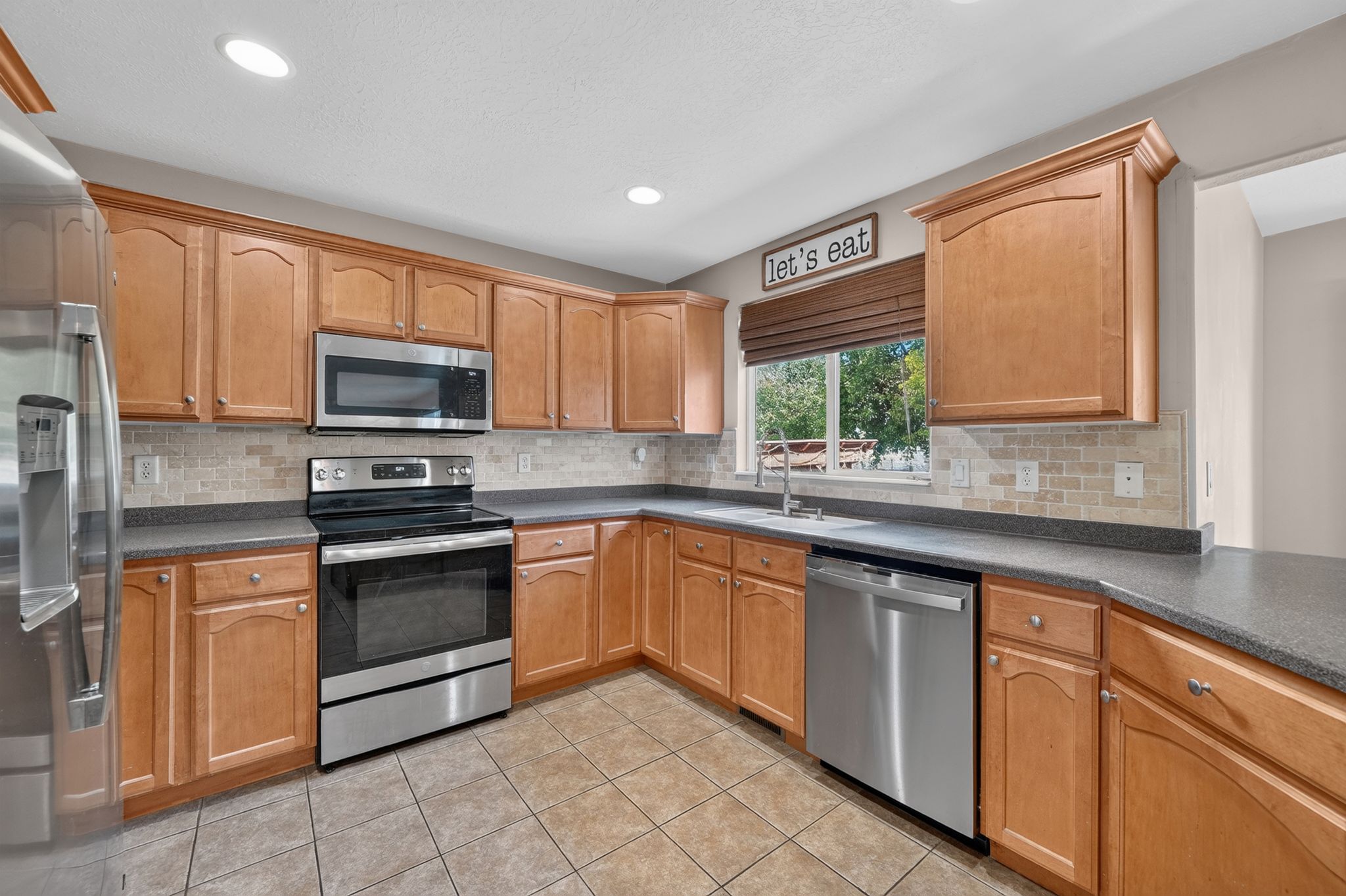 Kitchen featuring warm wood cabinetry, stainless steel appliances, speckled countertops, and a tiled backsplash