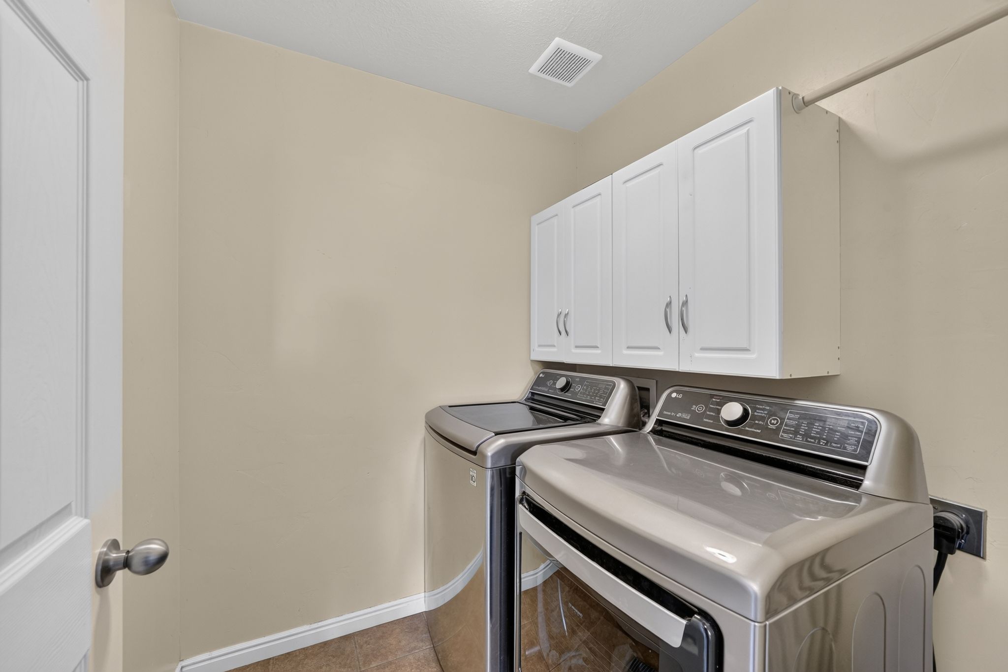 Laundry area featuring white shaker-style cabinetry, a white door with a brushed nickel knob, a wall-mounted drying rod, a ceiling vent, and light-toned walls