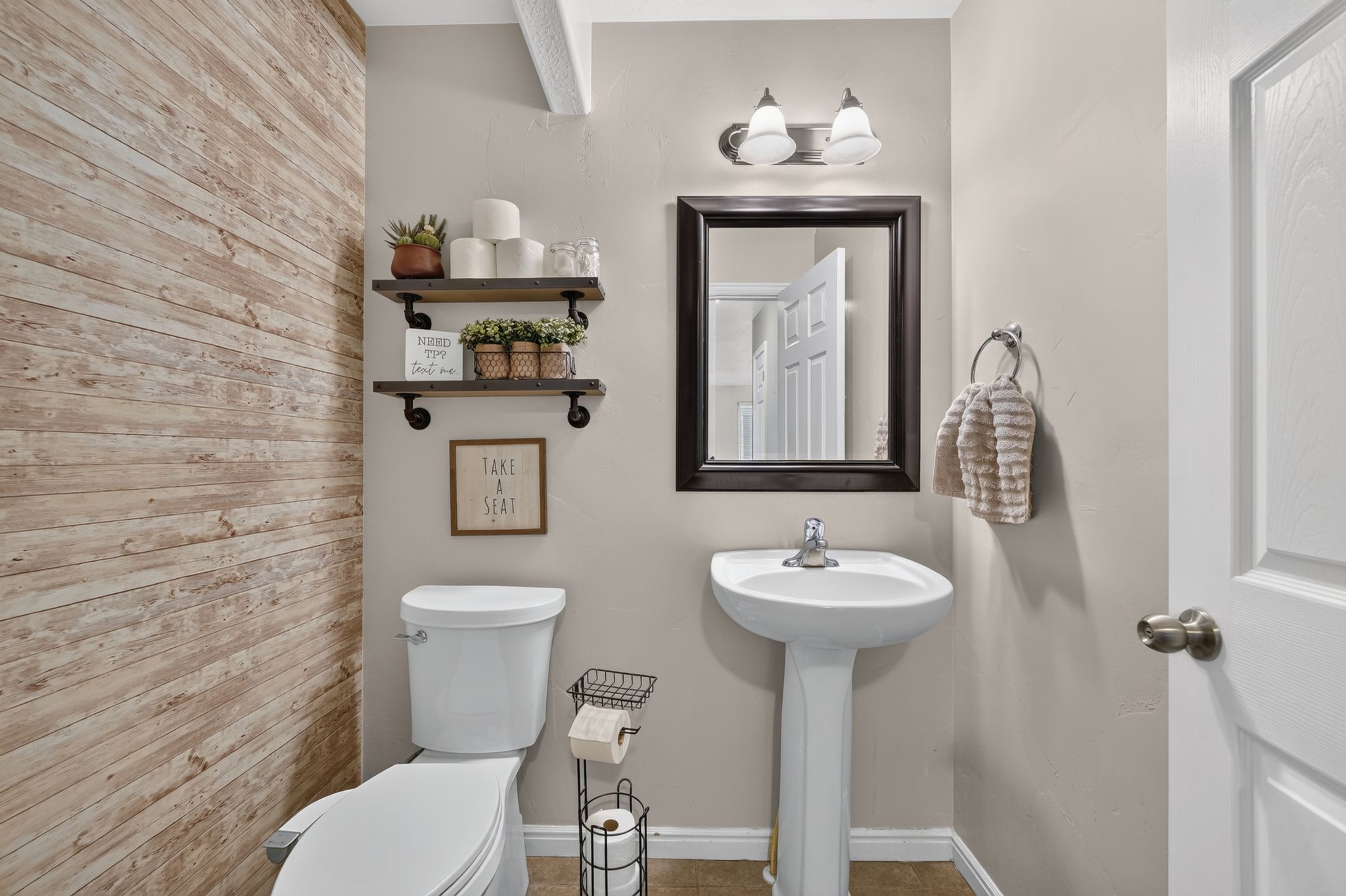 Bathroom featuring a wood-finish accent wall, pedestal sink, wall-mounted mirror, brushed nickel light fixture, and white interior door