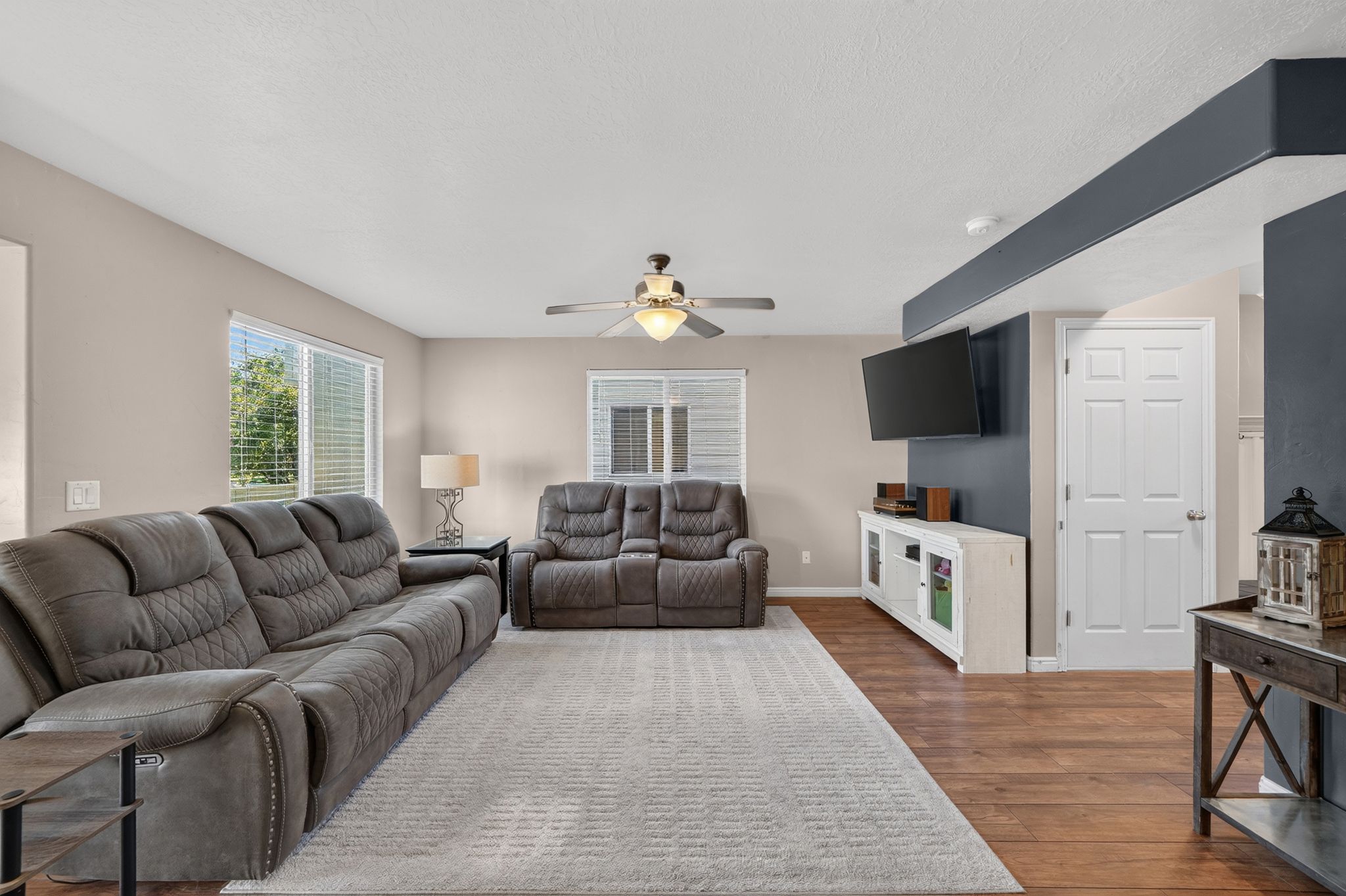 Spacious living area featuring light neutral wall tones, wood-finish flooring, and a ceiling fan with integrated lighting