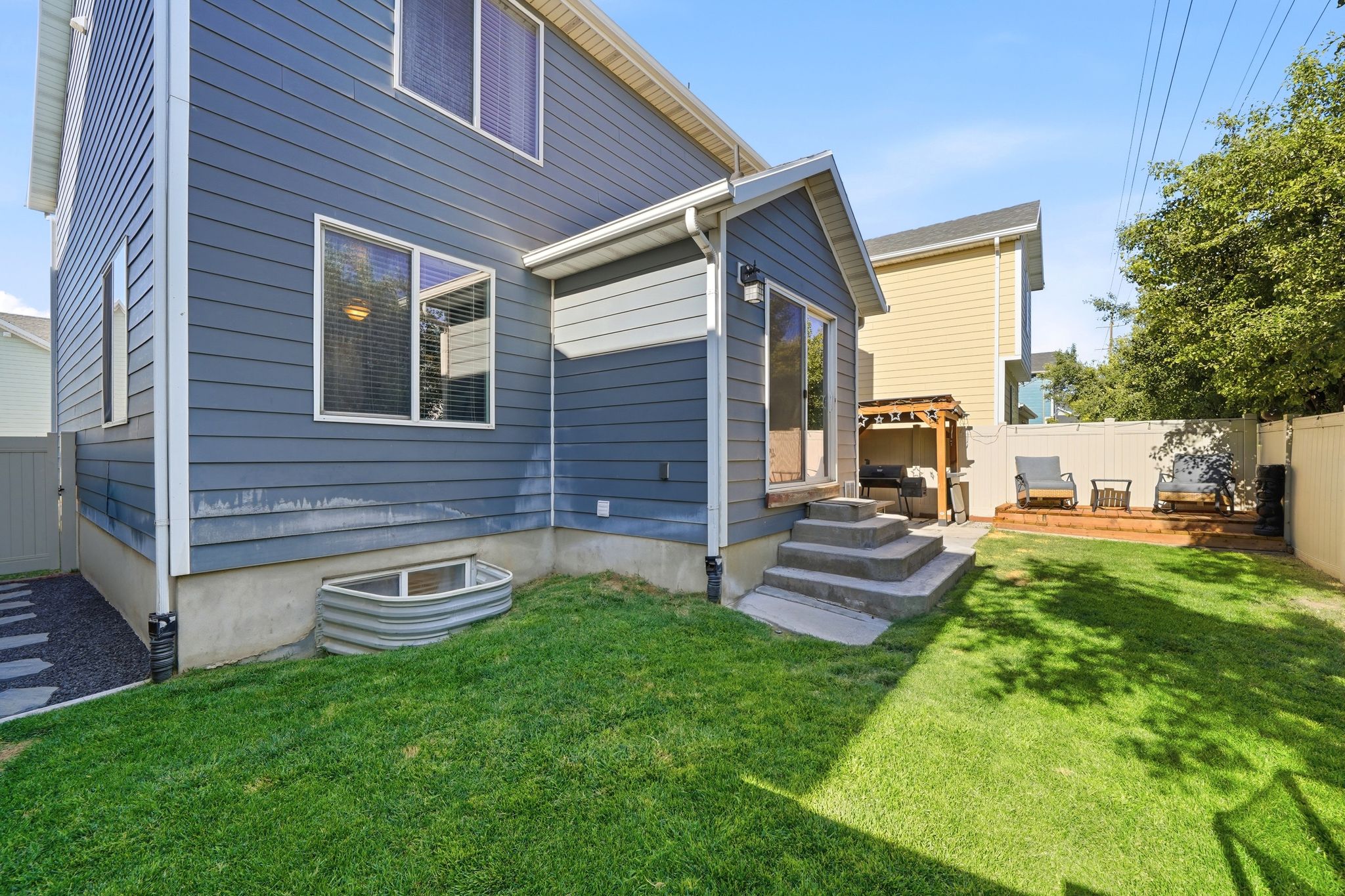 Rear exterior featuring blue siding, a manicured lawn, a concrete patio with steps, and a wooden deck