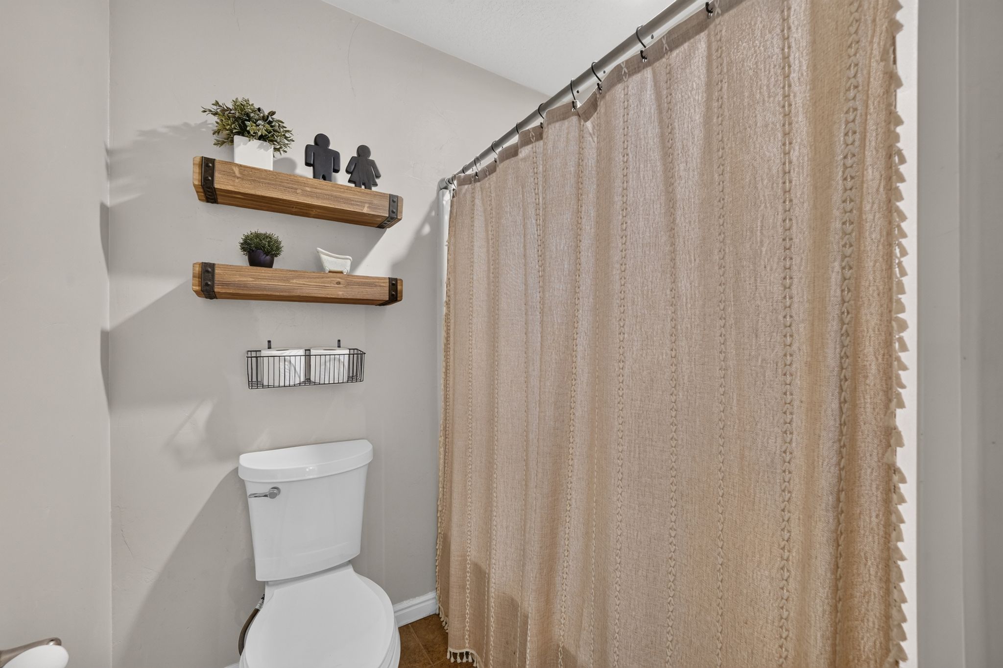 Full bathroom featuring a white toilet, two wood-finish floating shelves, and a fabric shower curtain on a metal rod