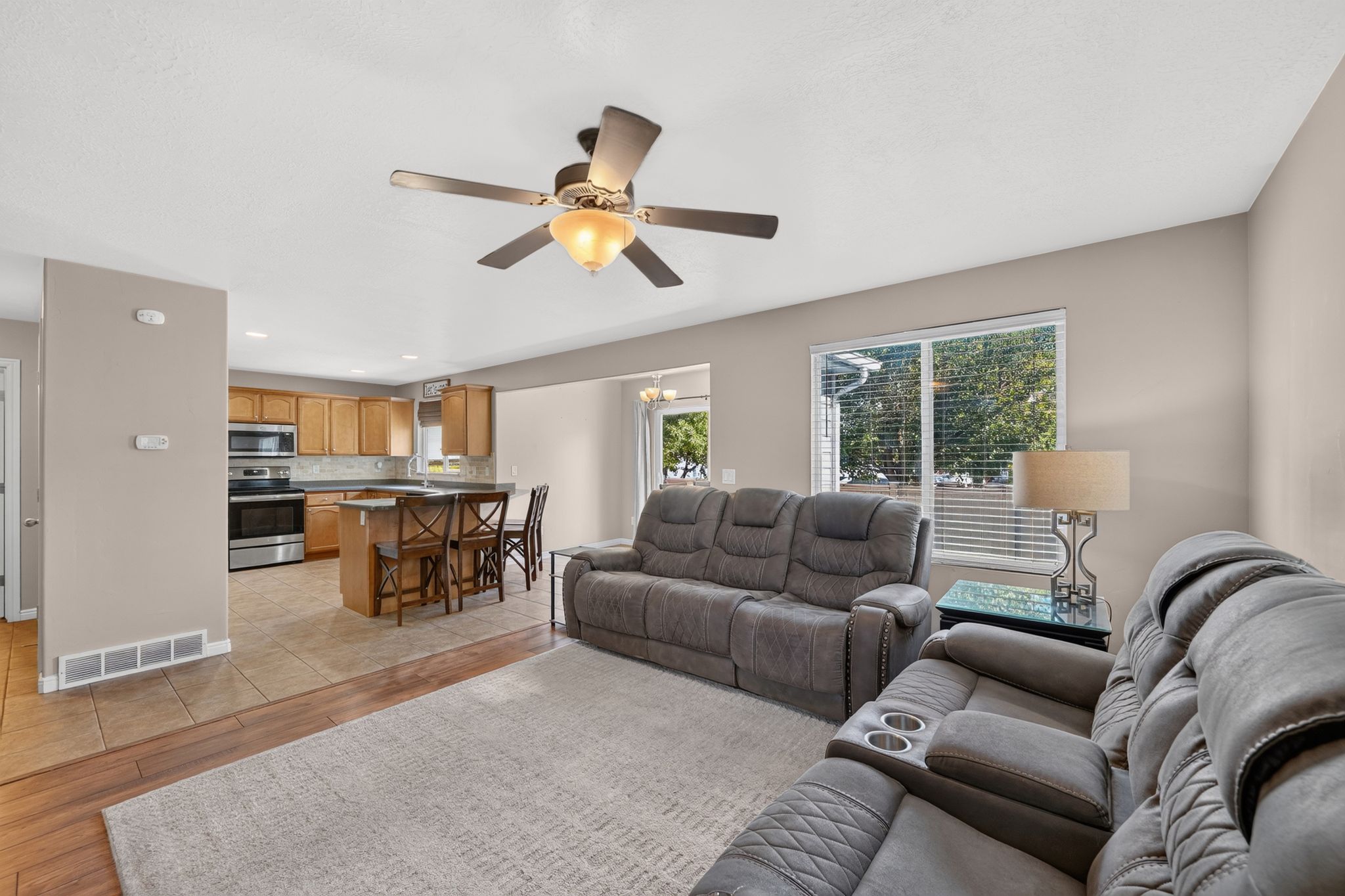 Spacious living area featuring a ceiling fan, a large window with blinds, and wood-finish flooring